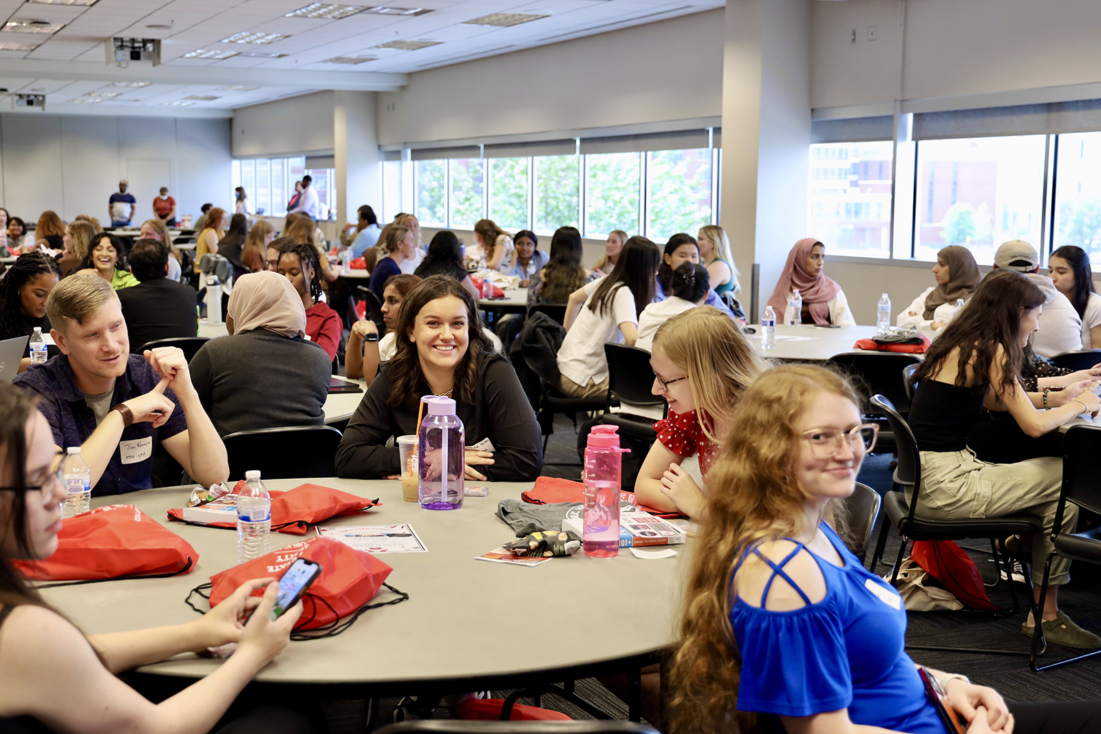 students sit around tables talking and smiling at orientation