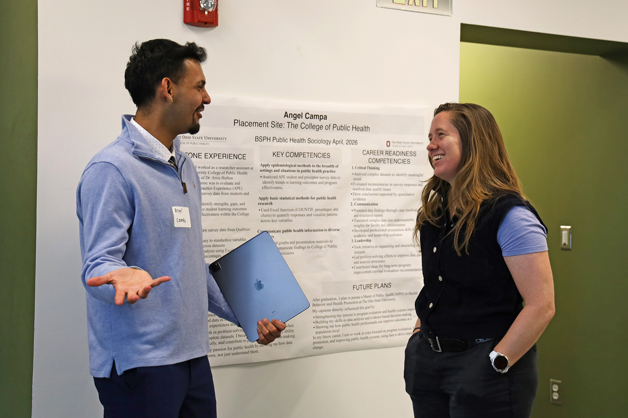 A student speaks with a faculty member in front of a poster about research.