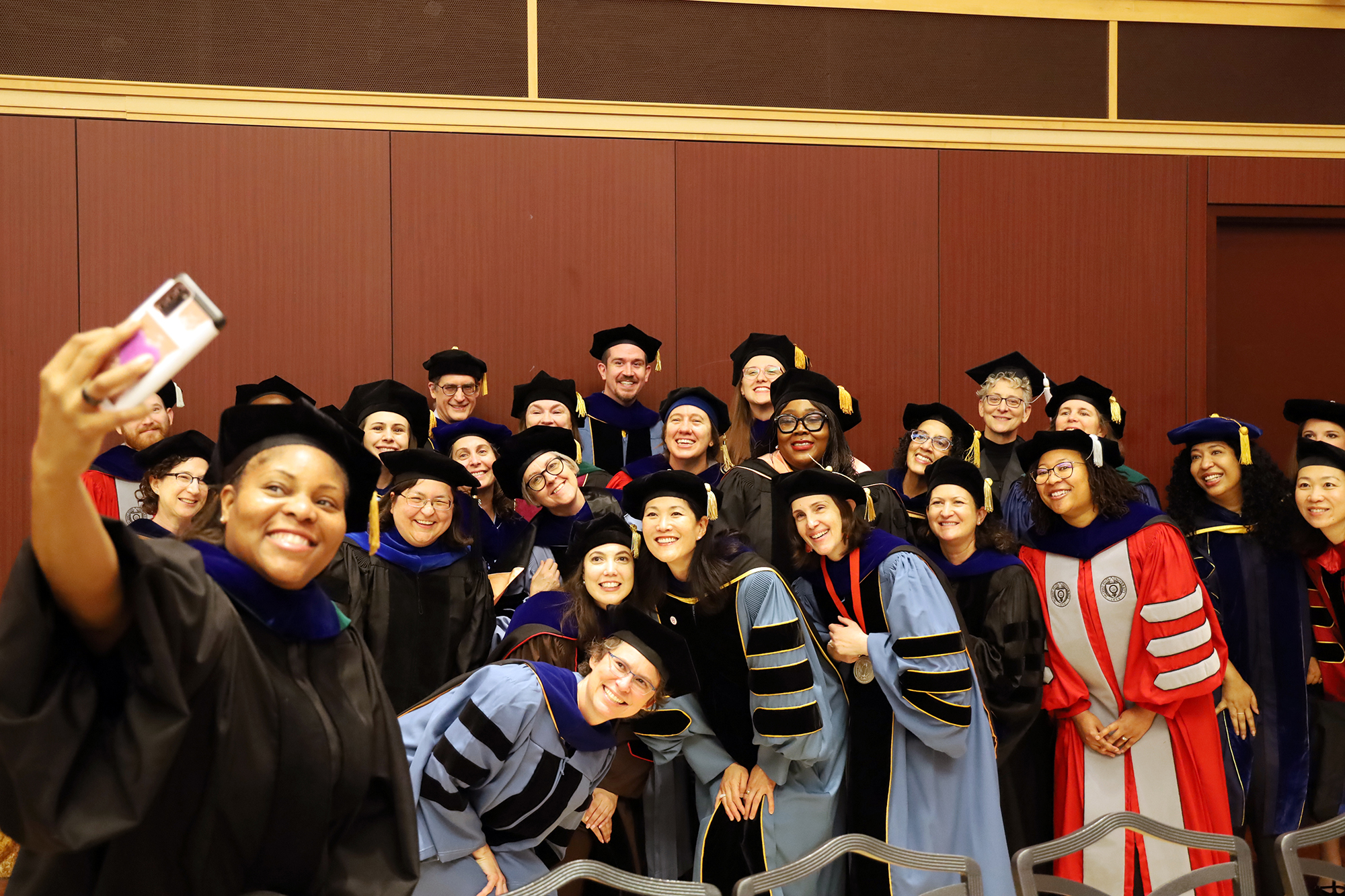 Faculty dressed in academic regalia snap a selfie