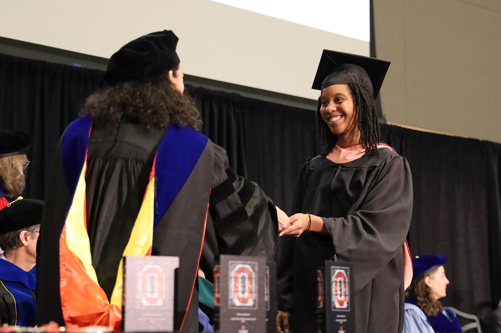 A student in academic regalia smiles while being handed a CPH medallion.. 