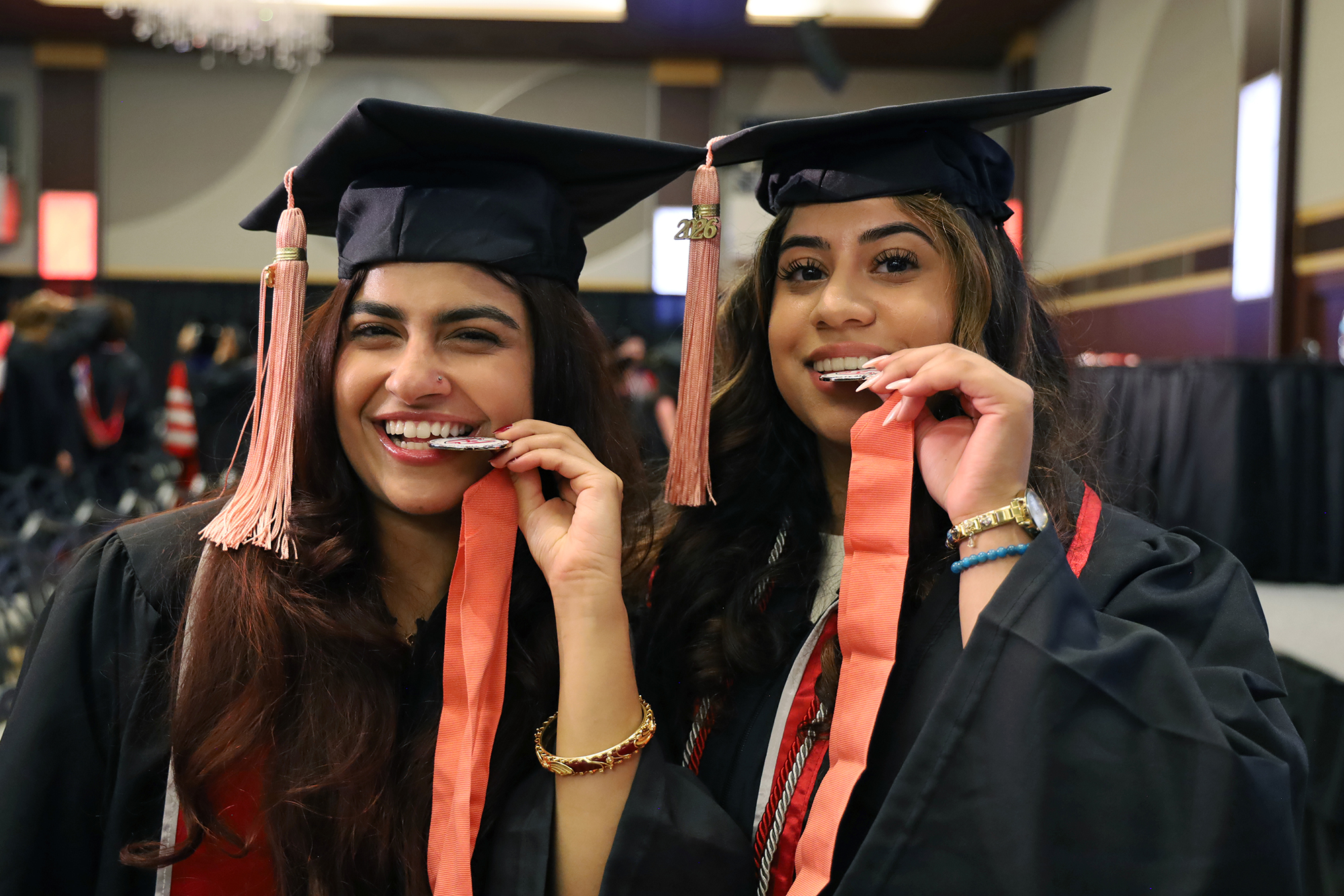 Two students in academic regalia bite their CPH medallions.