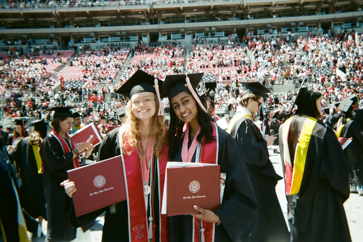 two student dressed in academic regalia hold diplomas.