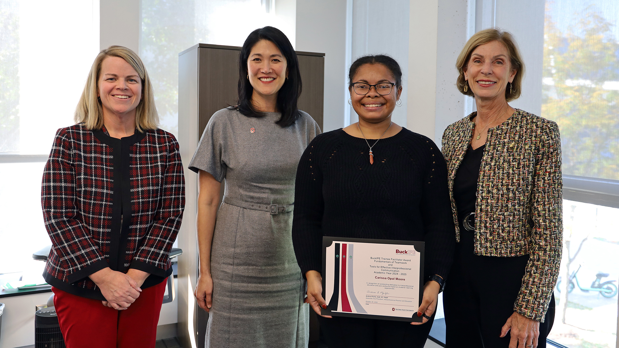 Four people smile. One person holds a certificate.