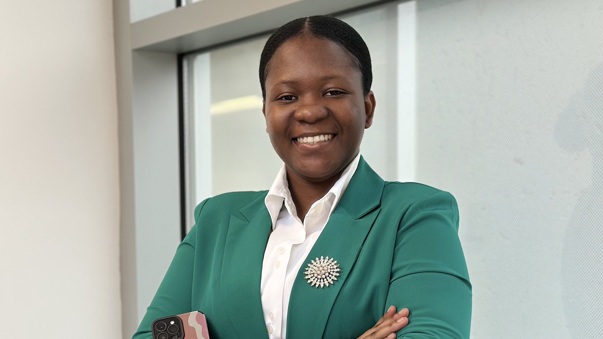 A student wearing a green blazer with a brooch and a white shirt smiles