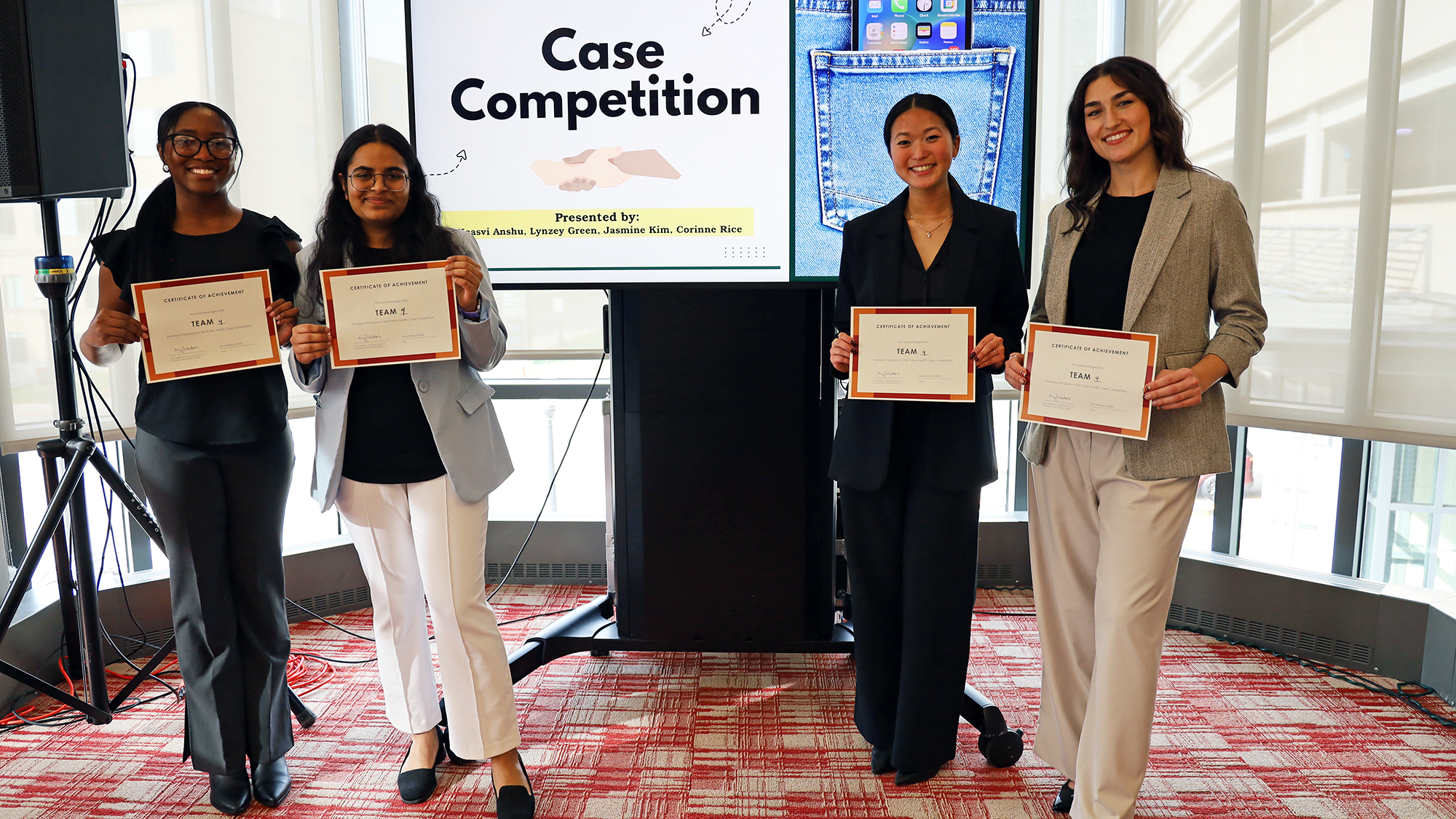 Four people dressed in business attire pose with certificates