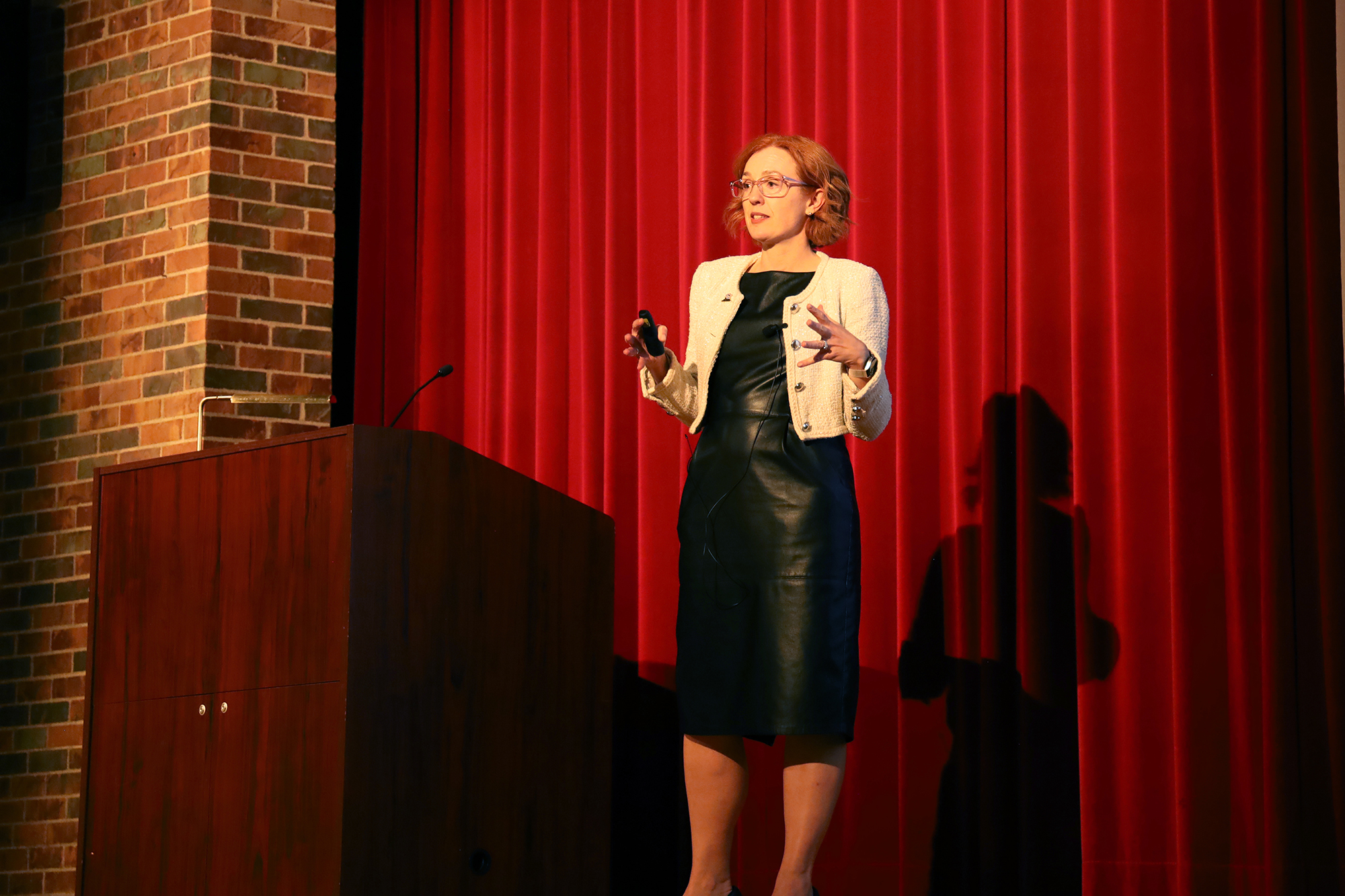 Emmy Betz speaks to an audience in front of a red curtain background.