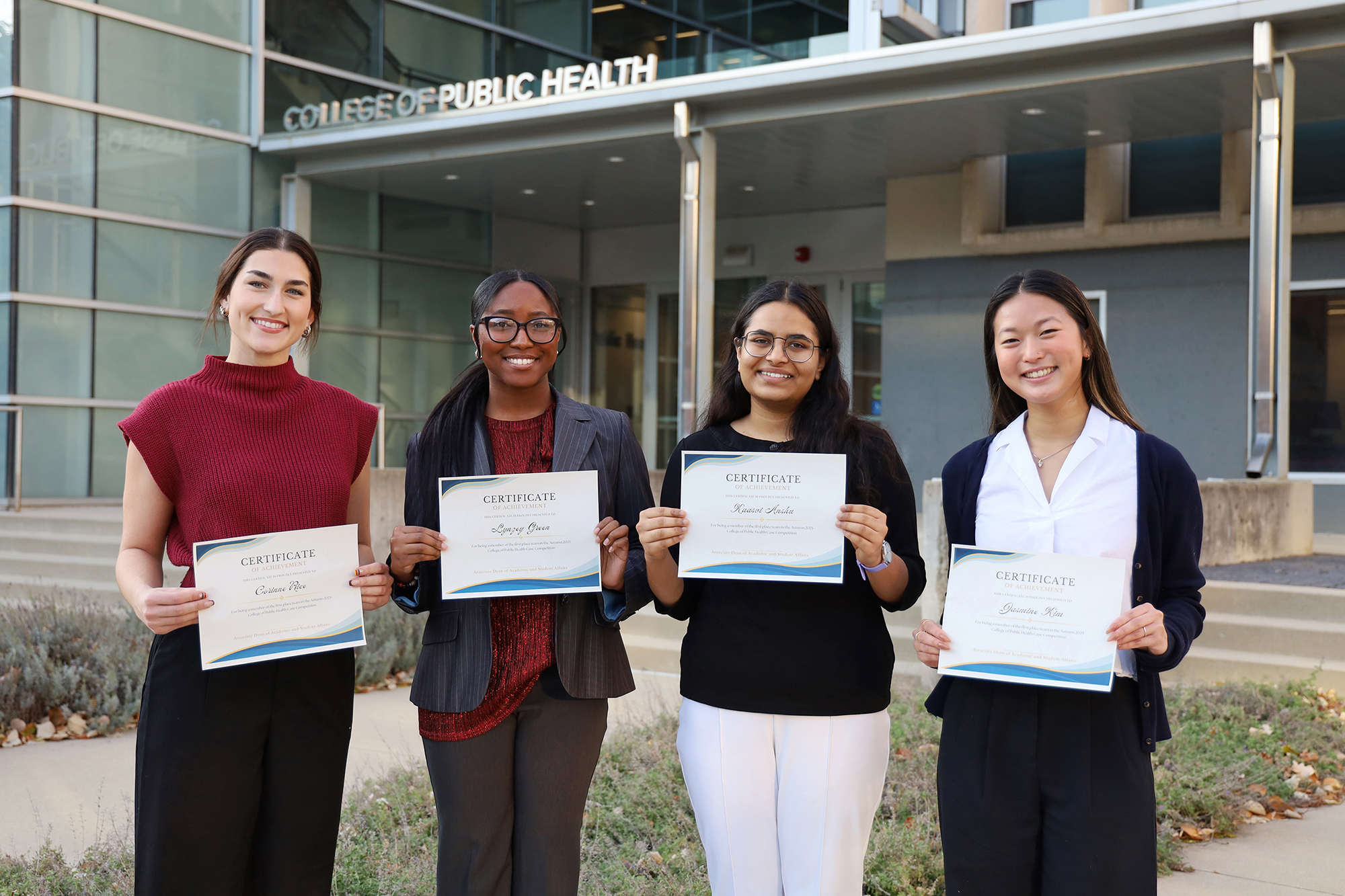 Four students hold certificates in front of Cunz Hall.