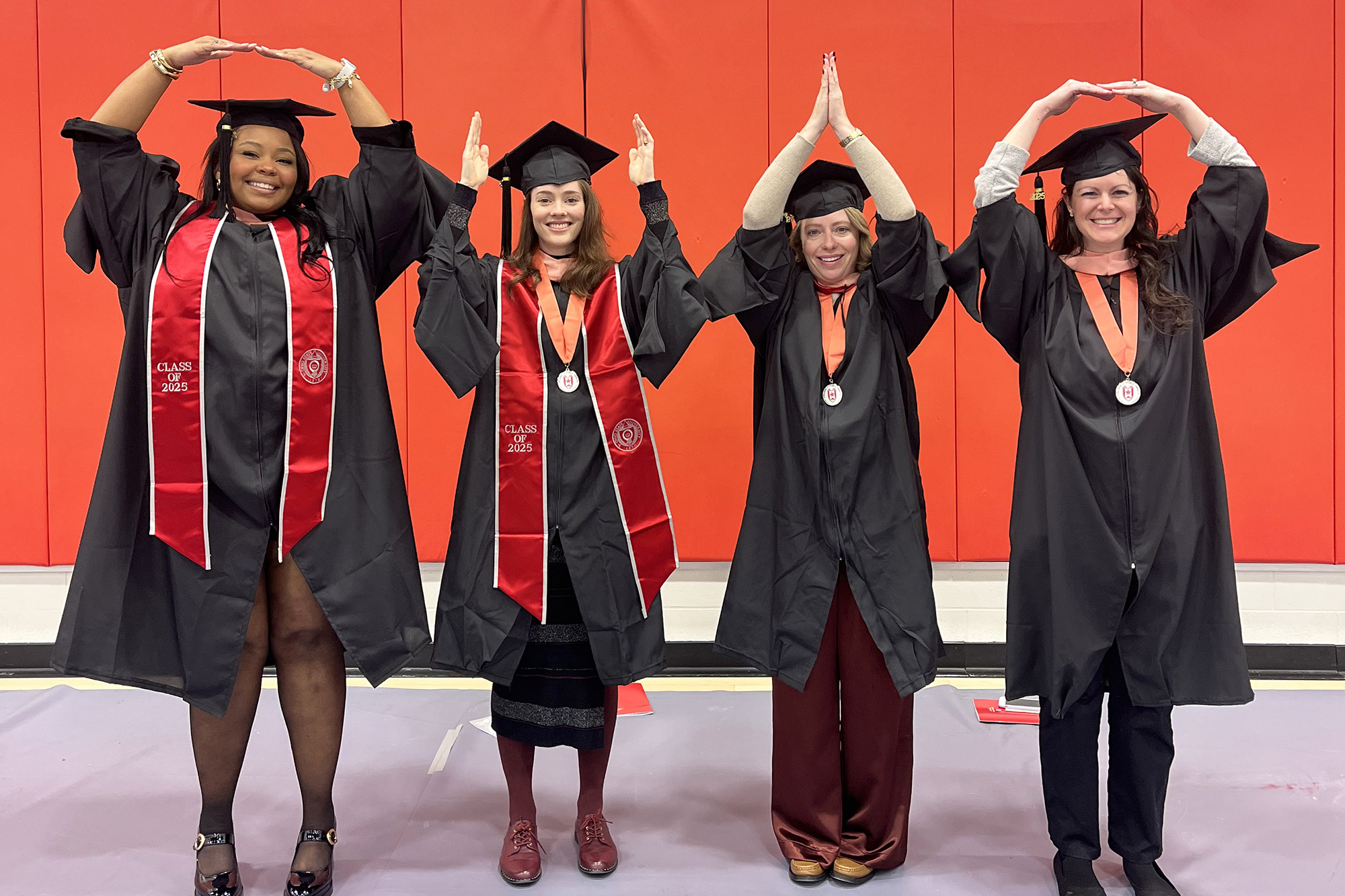 Four students in graduation robes spell out "O-H-I-O" with this arms.