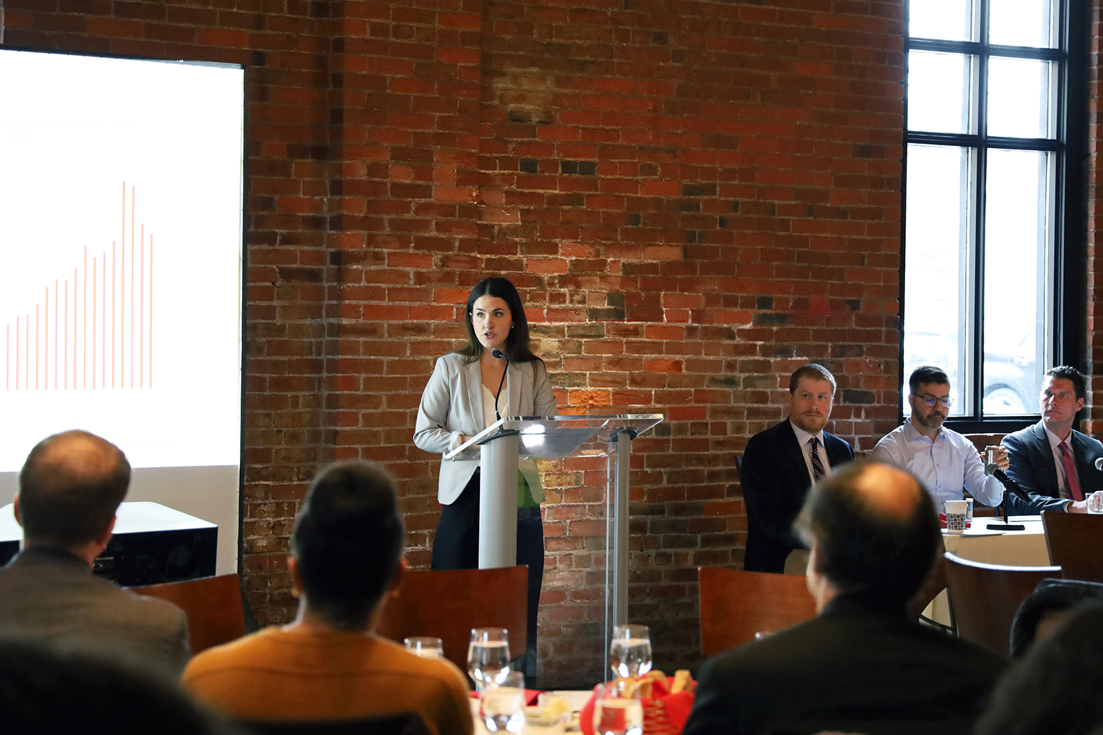 Laura Prater speaks at a lectern in front of people seated at tables.