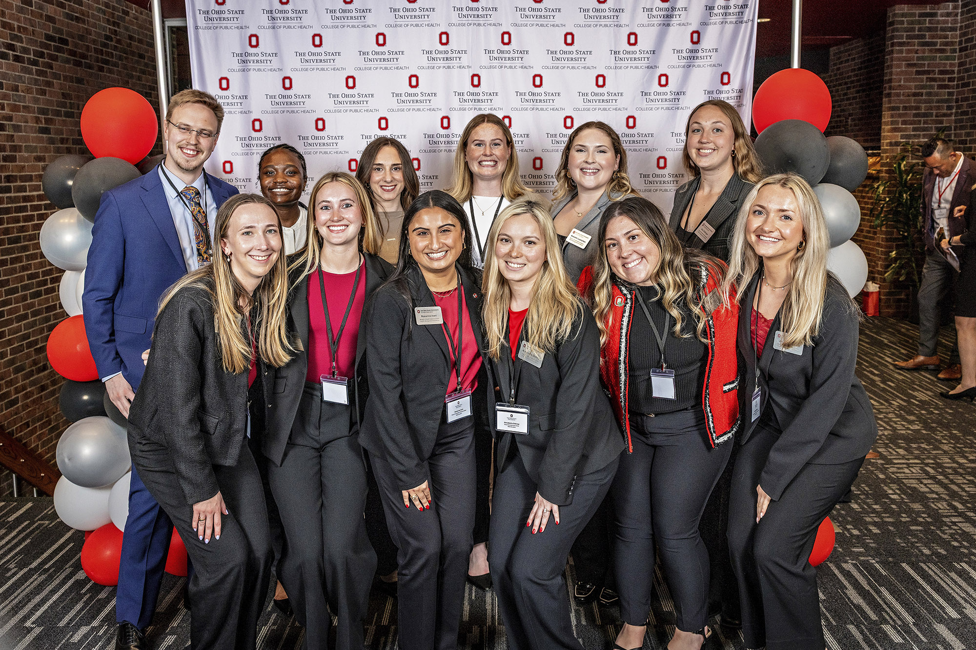 Students in business attire smile in front of an Ohio State backdrop with balloons.