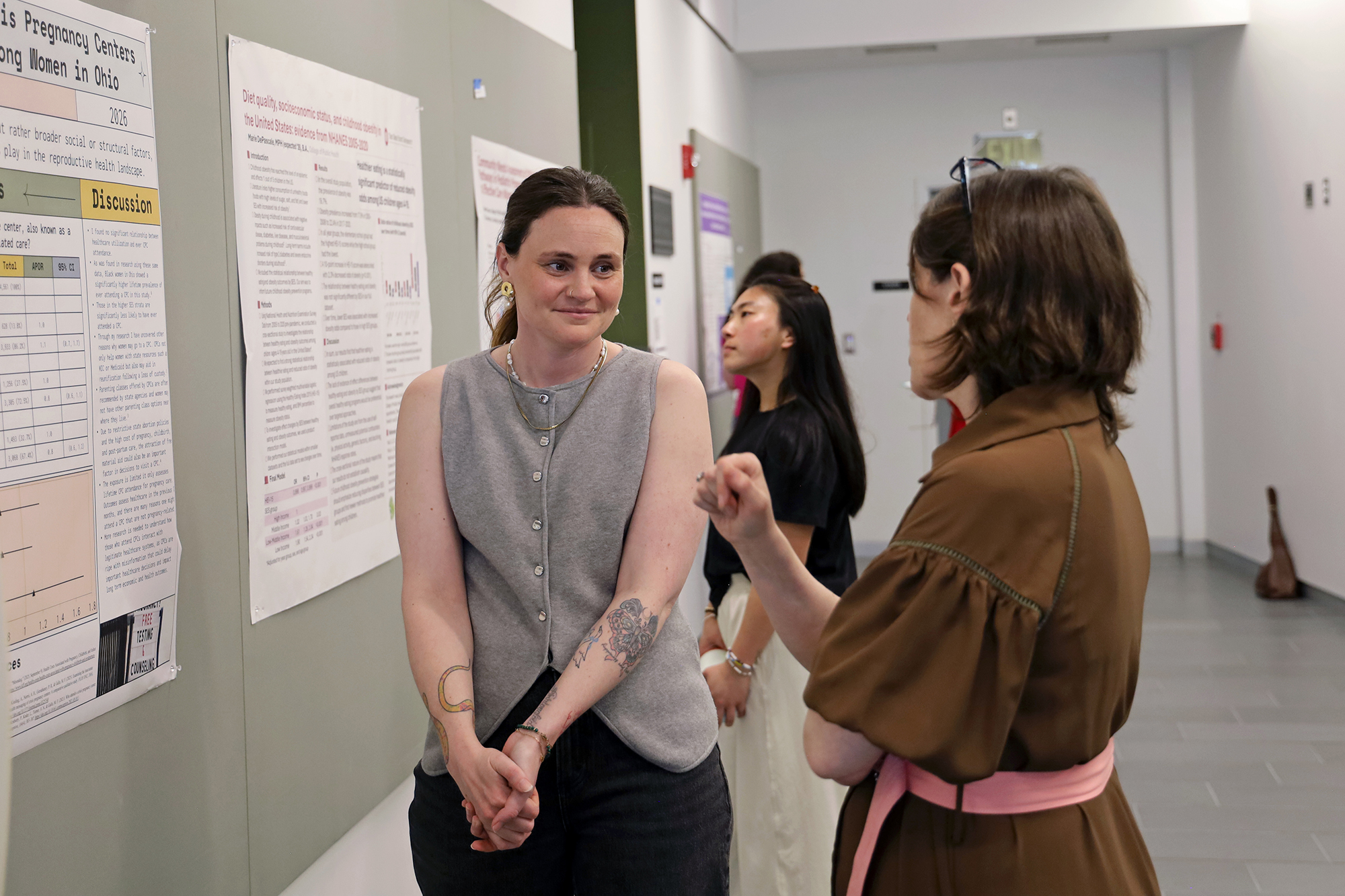 A graduate students speaks with someone next to a poster about research.