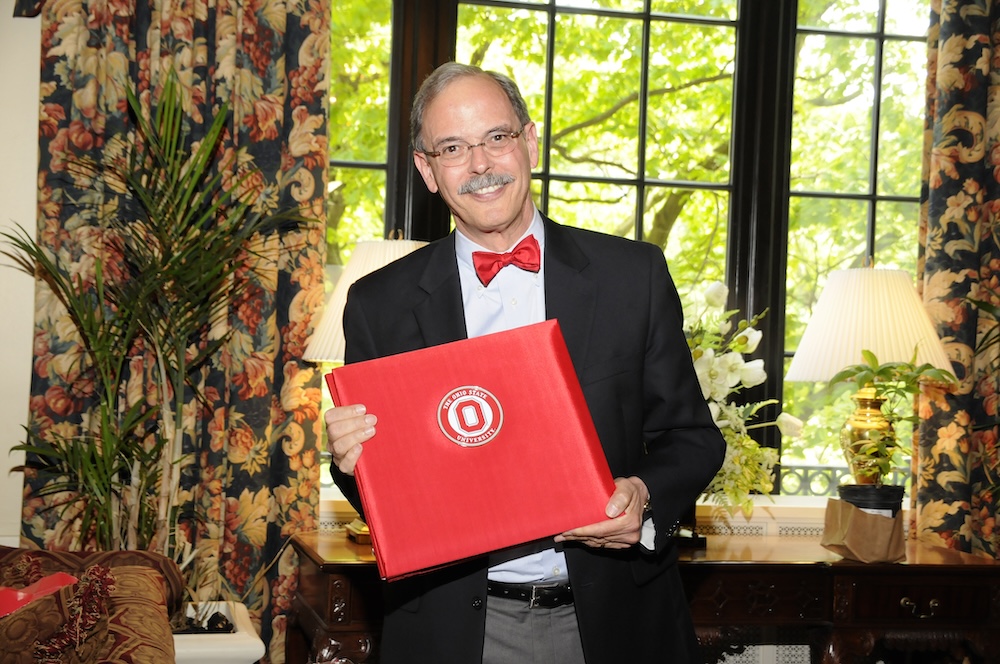 Jeff Caswell stands in an office holding a diploma