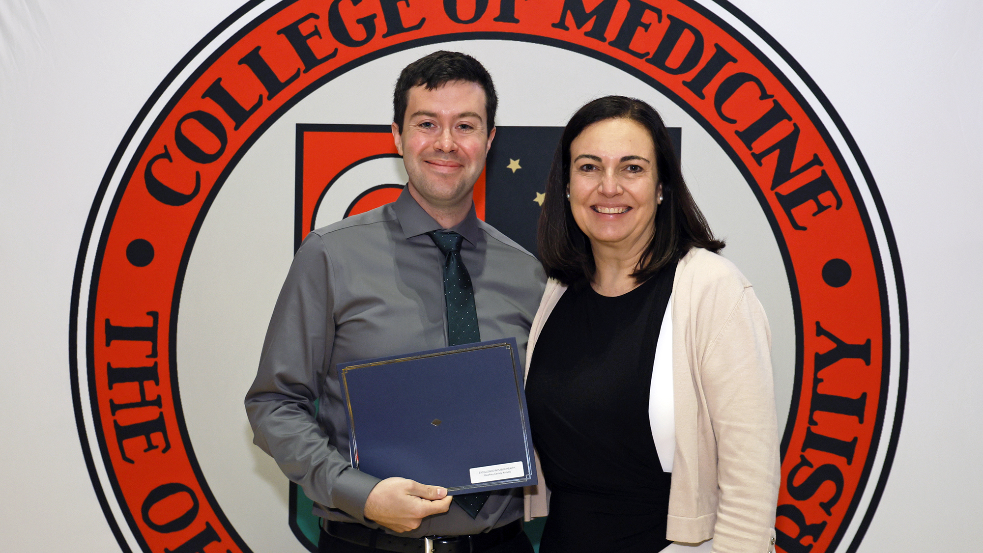 A person holds a certificate in a folder with the College of Medicine seal in the background.