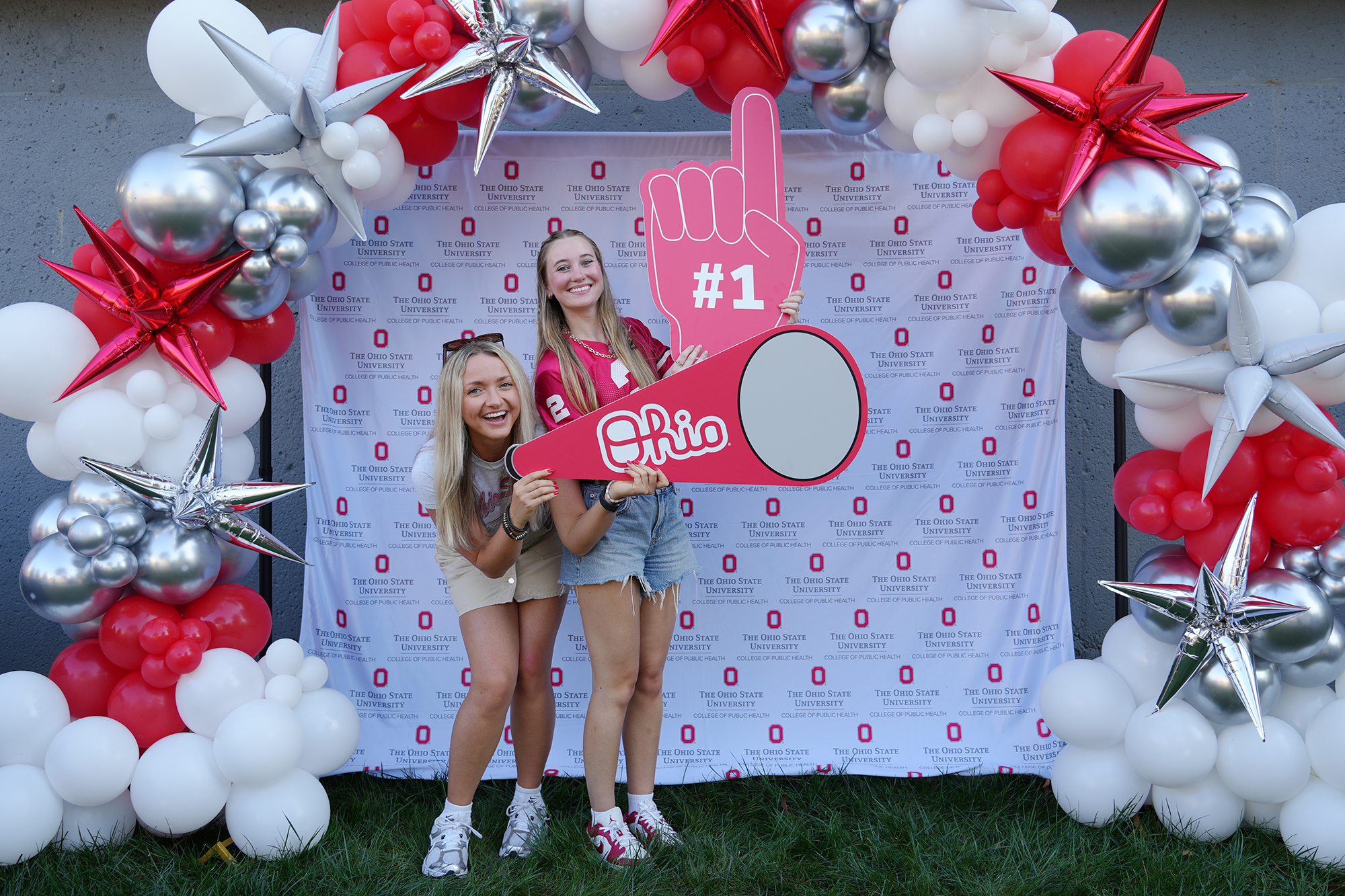 Two people with Ohio State props stand in front of an Ohio State backdrop.
