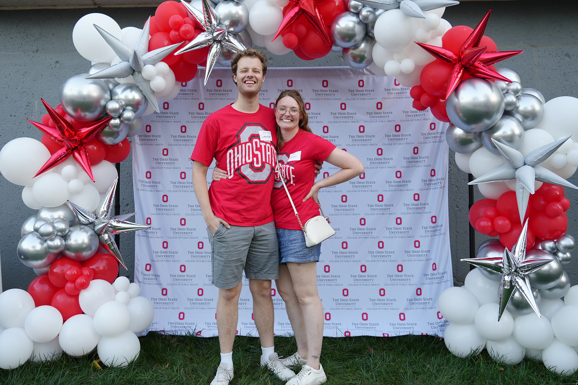 two people stand in front of an Ohio State background. They are wearing red Ohio State shirts.