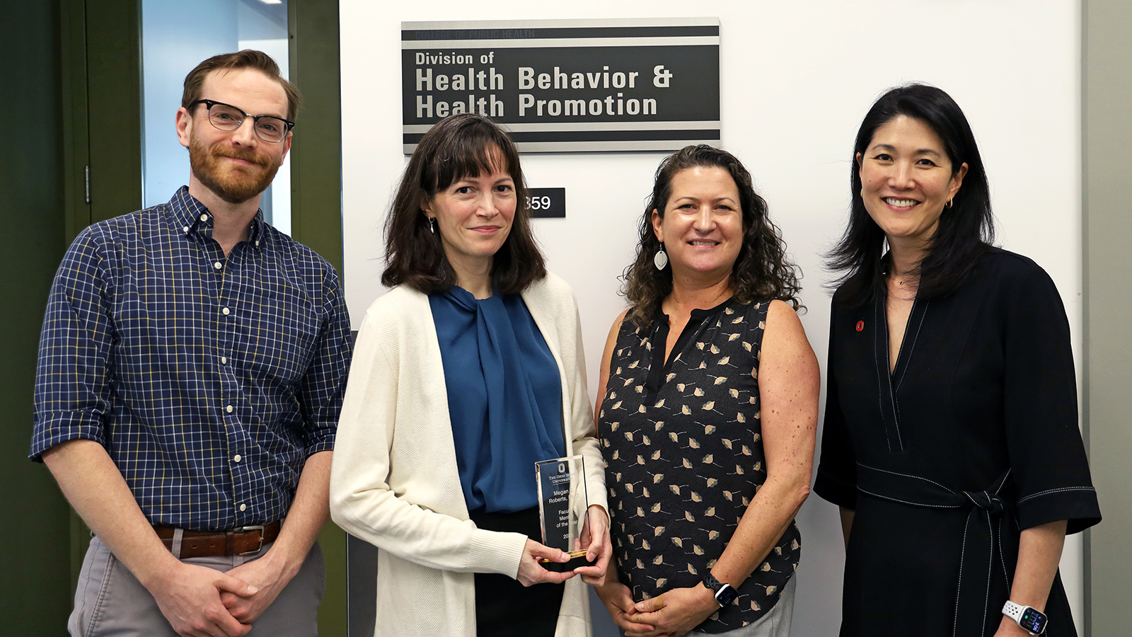 Four people stand together for a photo. One person holds a glass award.