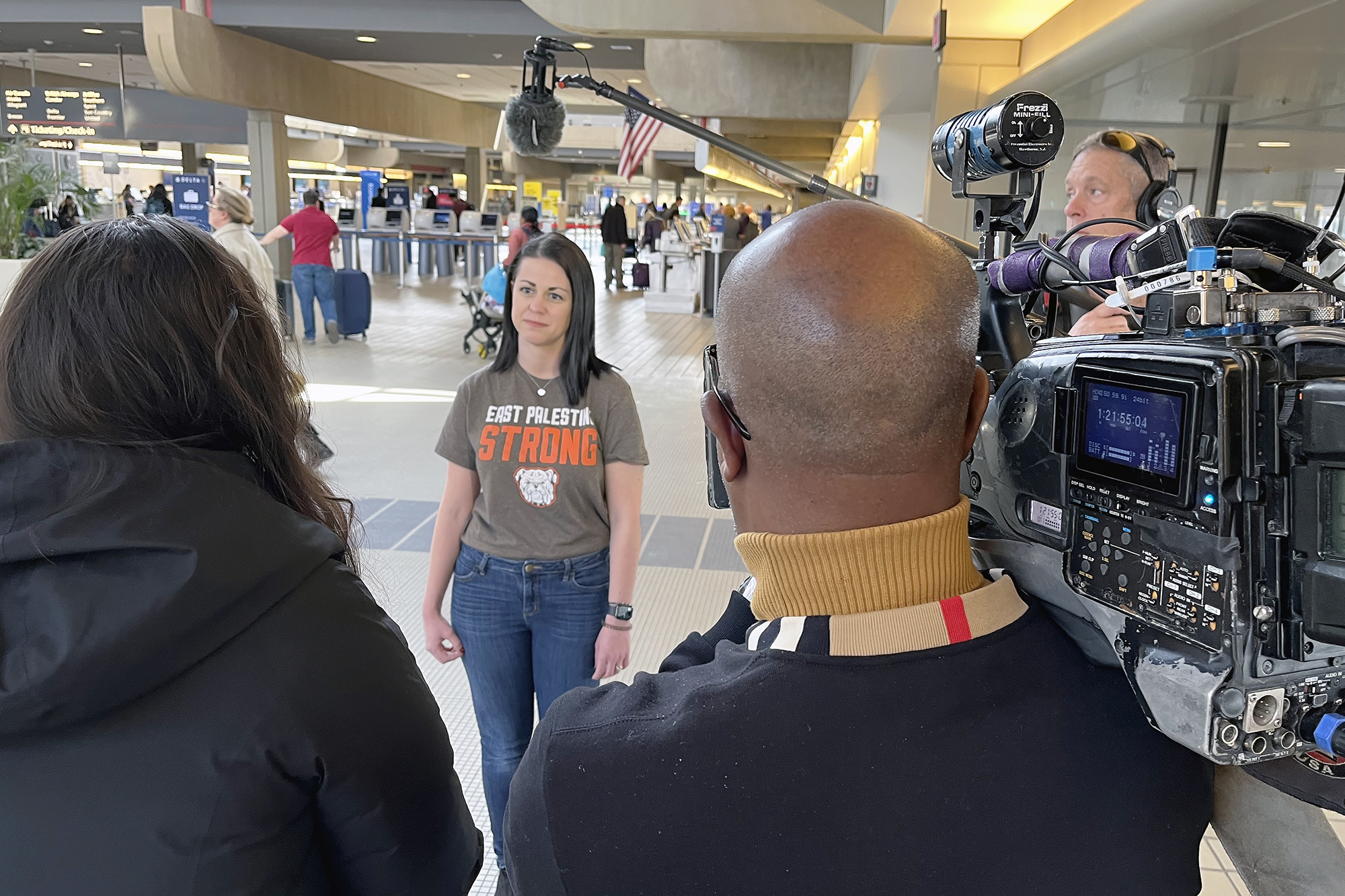 Misti Allison stands in front of people pointing a TV camera and microphone at her.