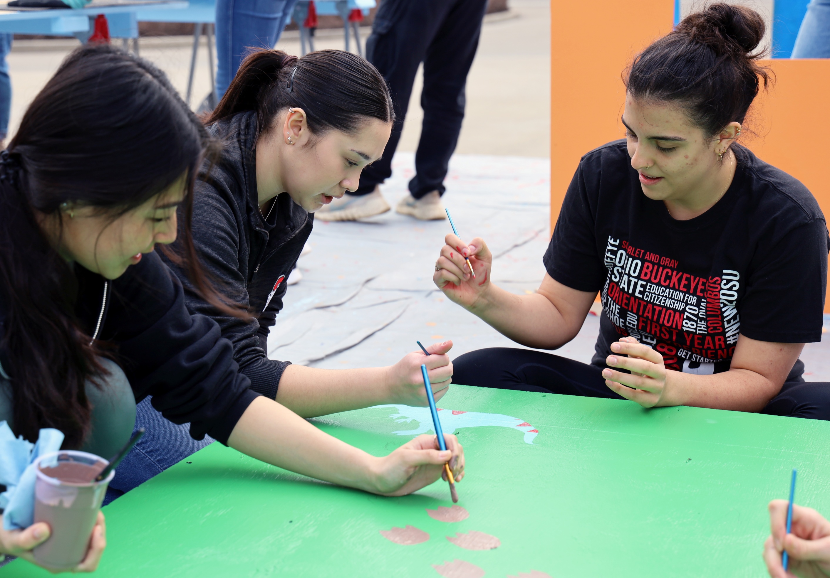 Students paint dinosaurs on a green background