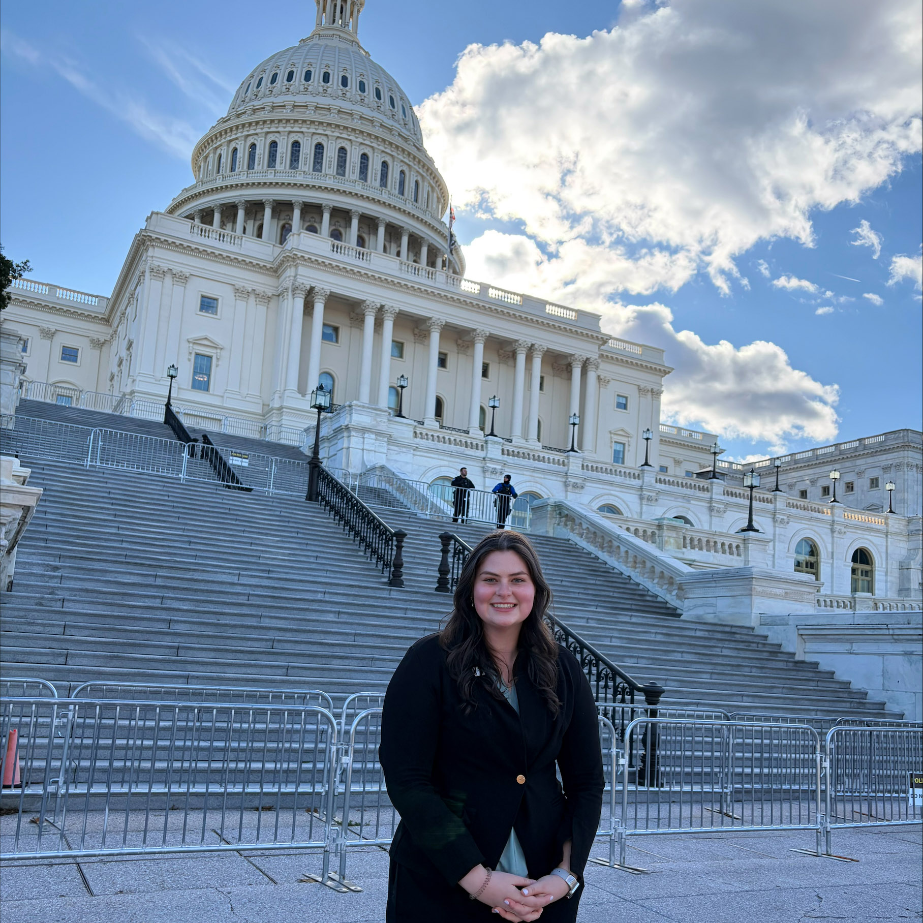 A student in professional attire smiles with the U.S. Capitol building in the background.