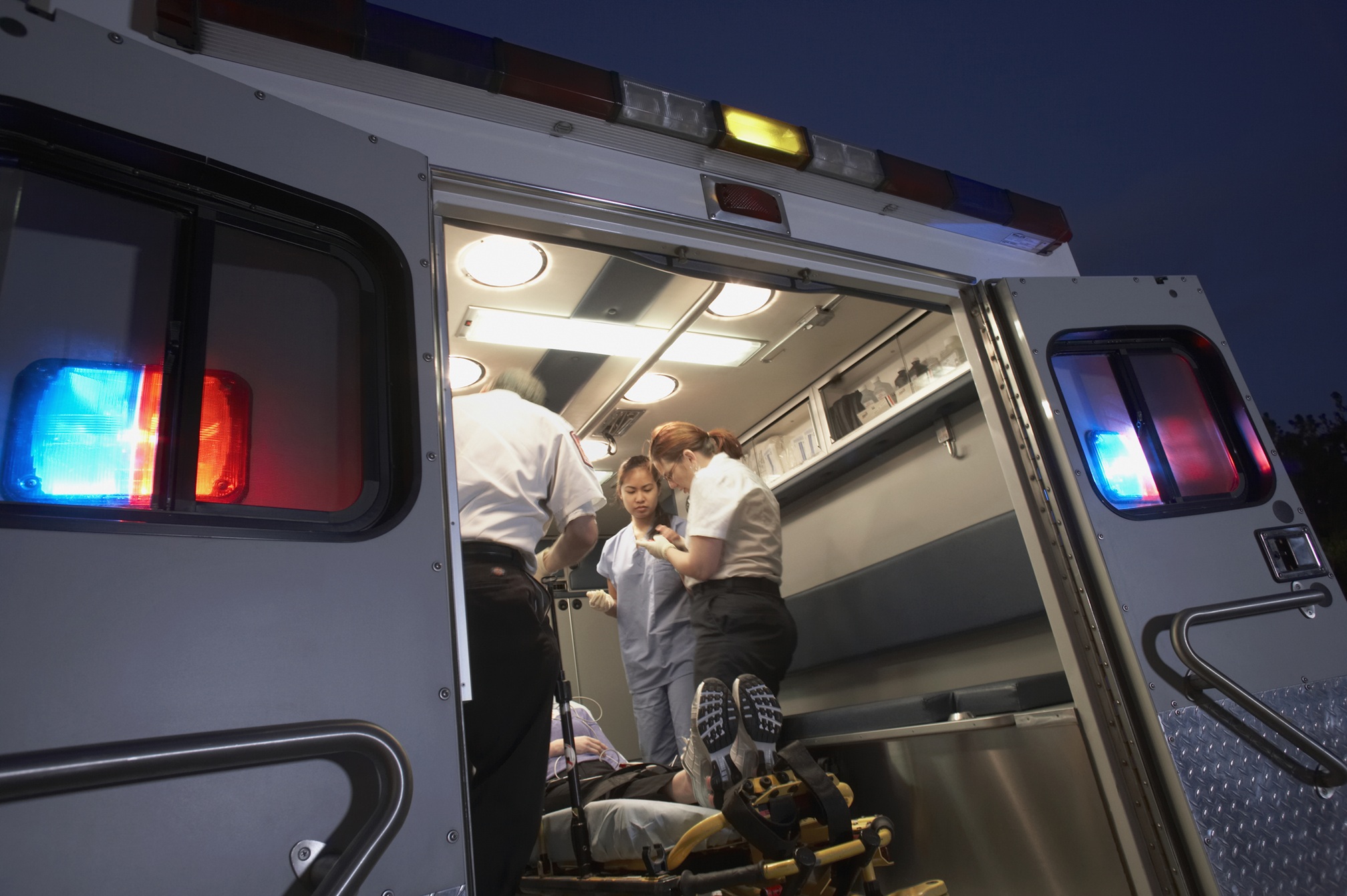 an ambulance at night wiht hte doors open and a patient and caregivers inside