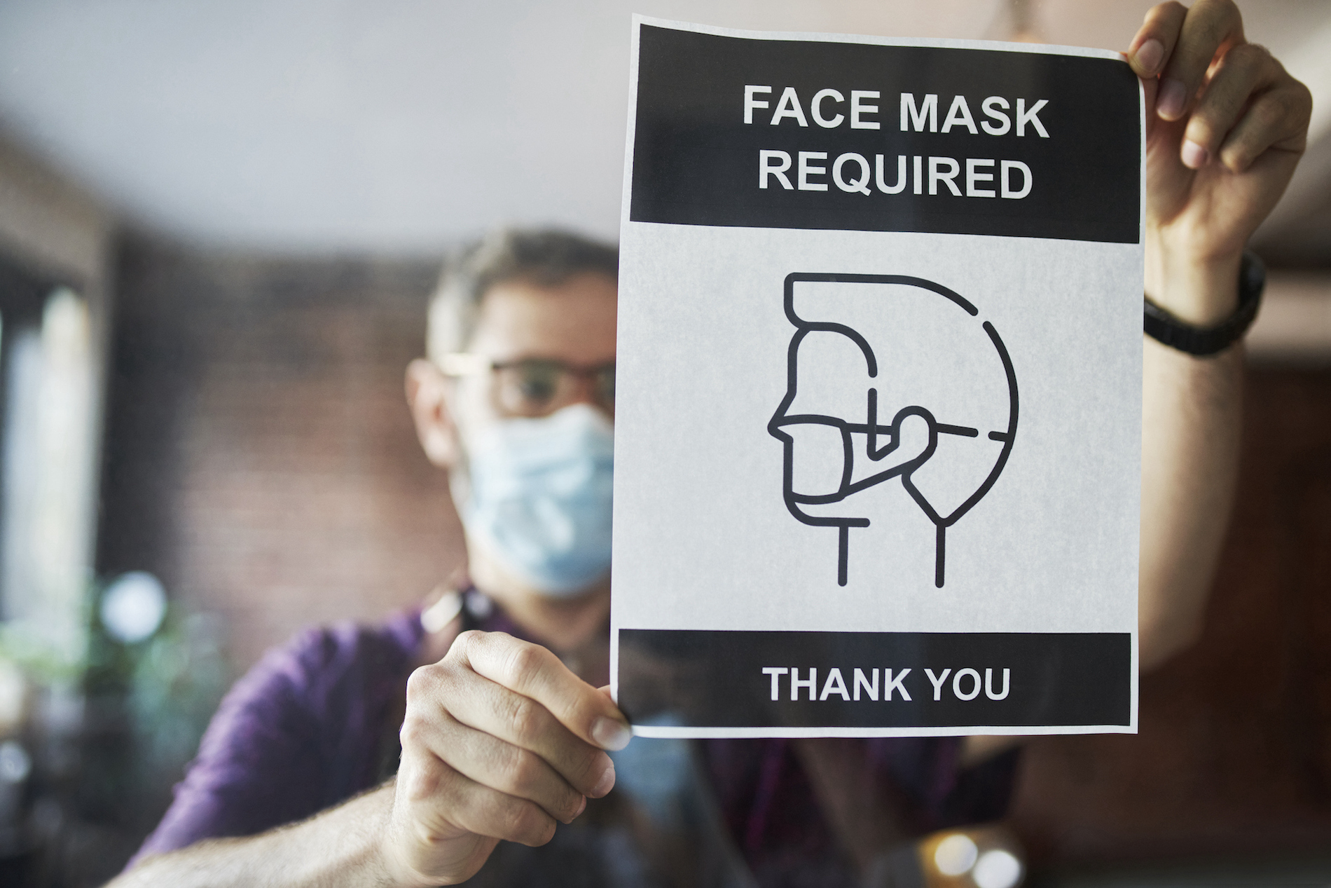Man posting a sign that says masks are required