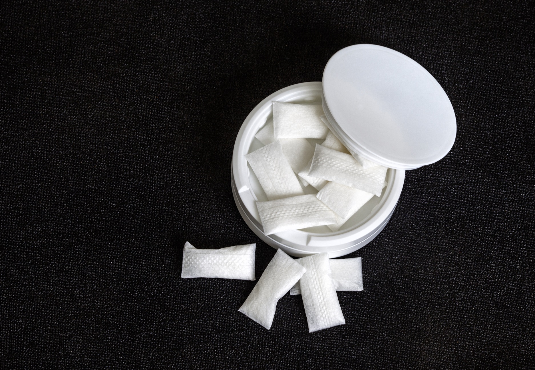 A black background with a white tin full of white nicotine pouches