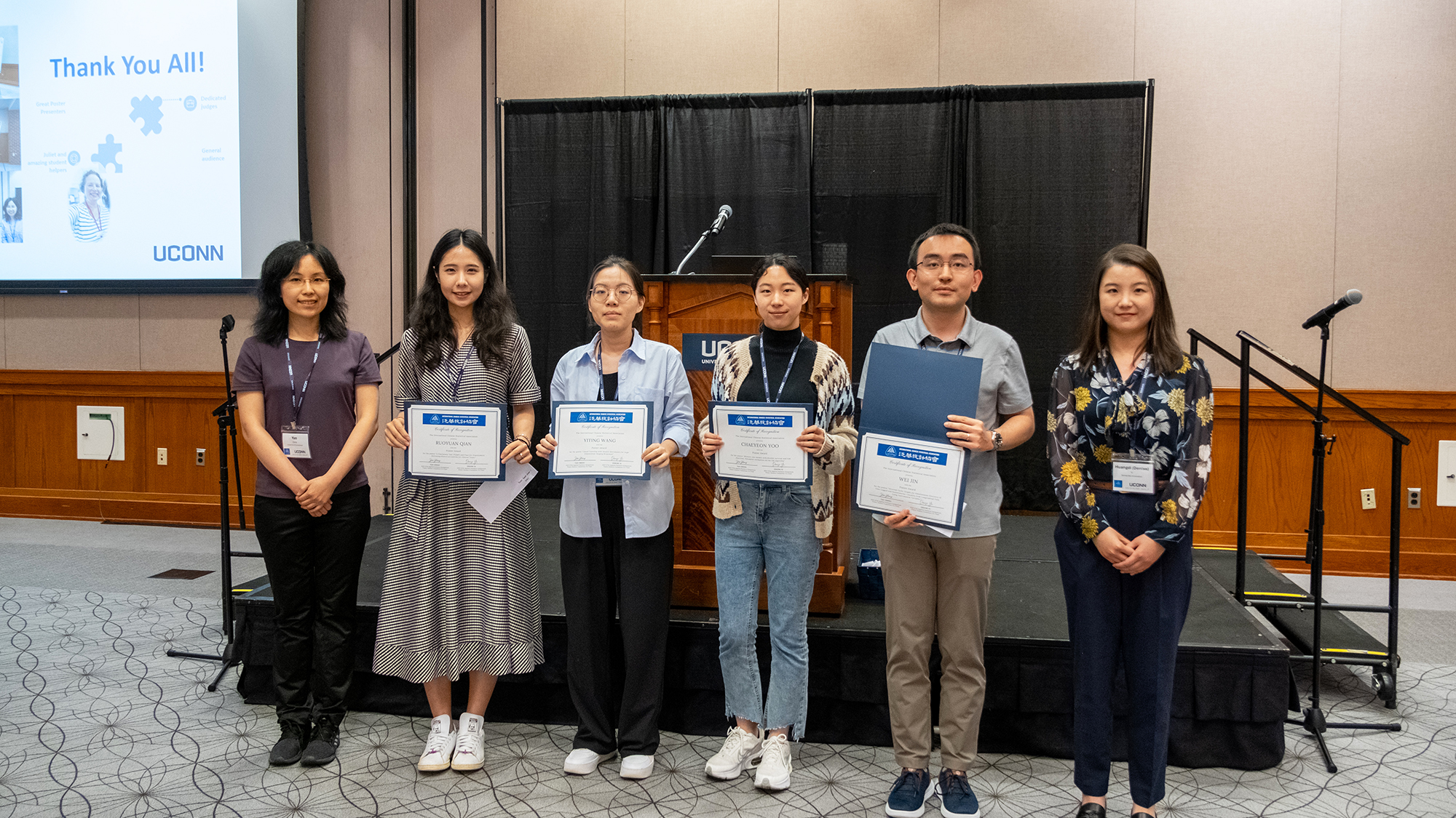 Six people pose for a photo, four of them hold certificates.