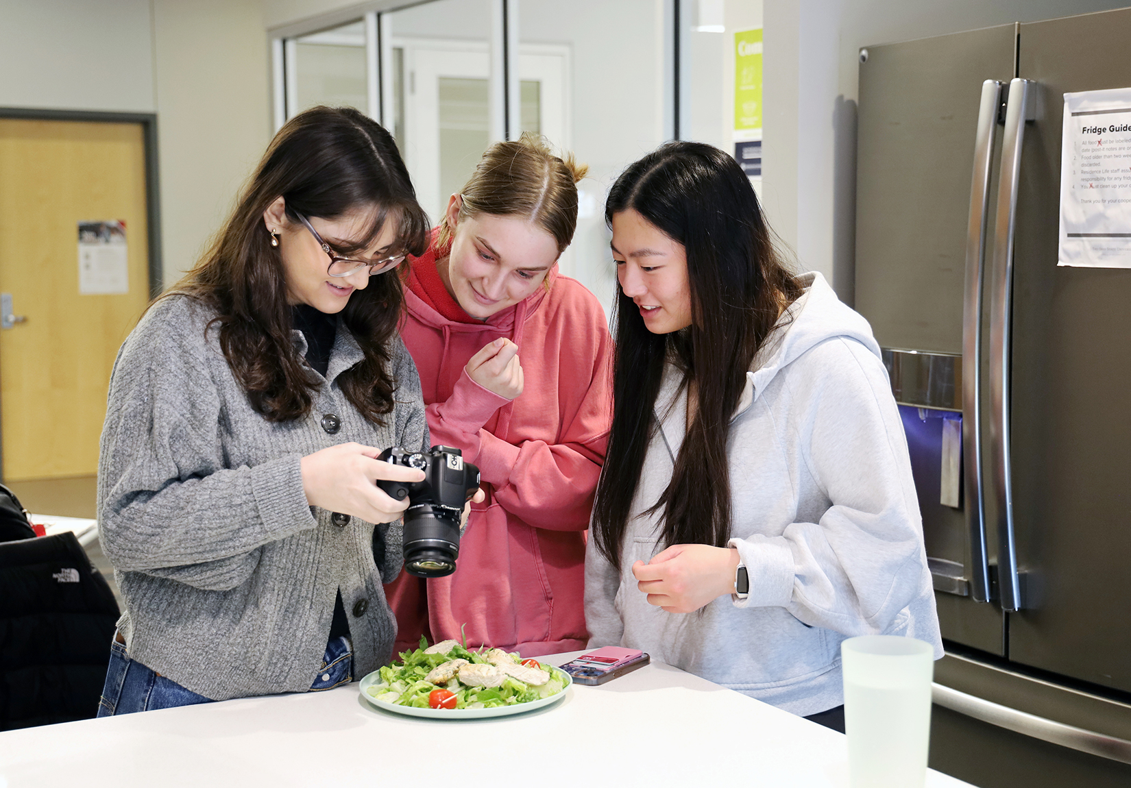 Three students look at a camera in the Nosker House kitchen