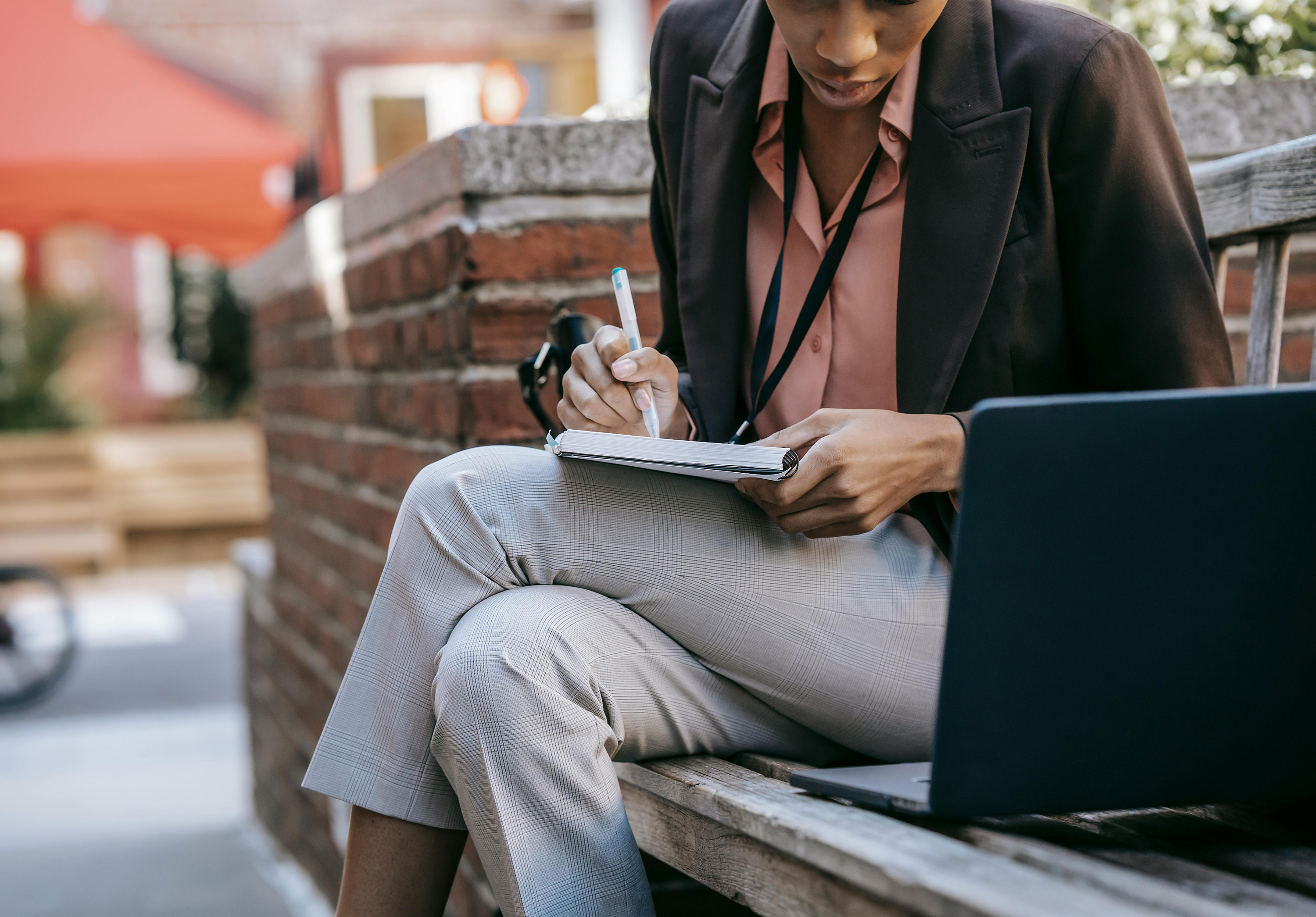person writing in a notebook in front of a laptop