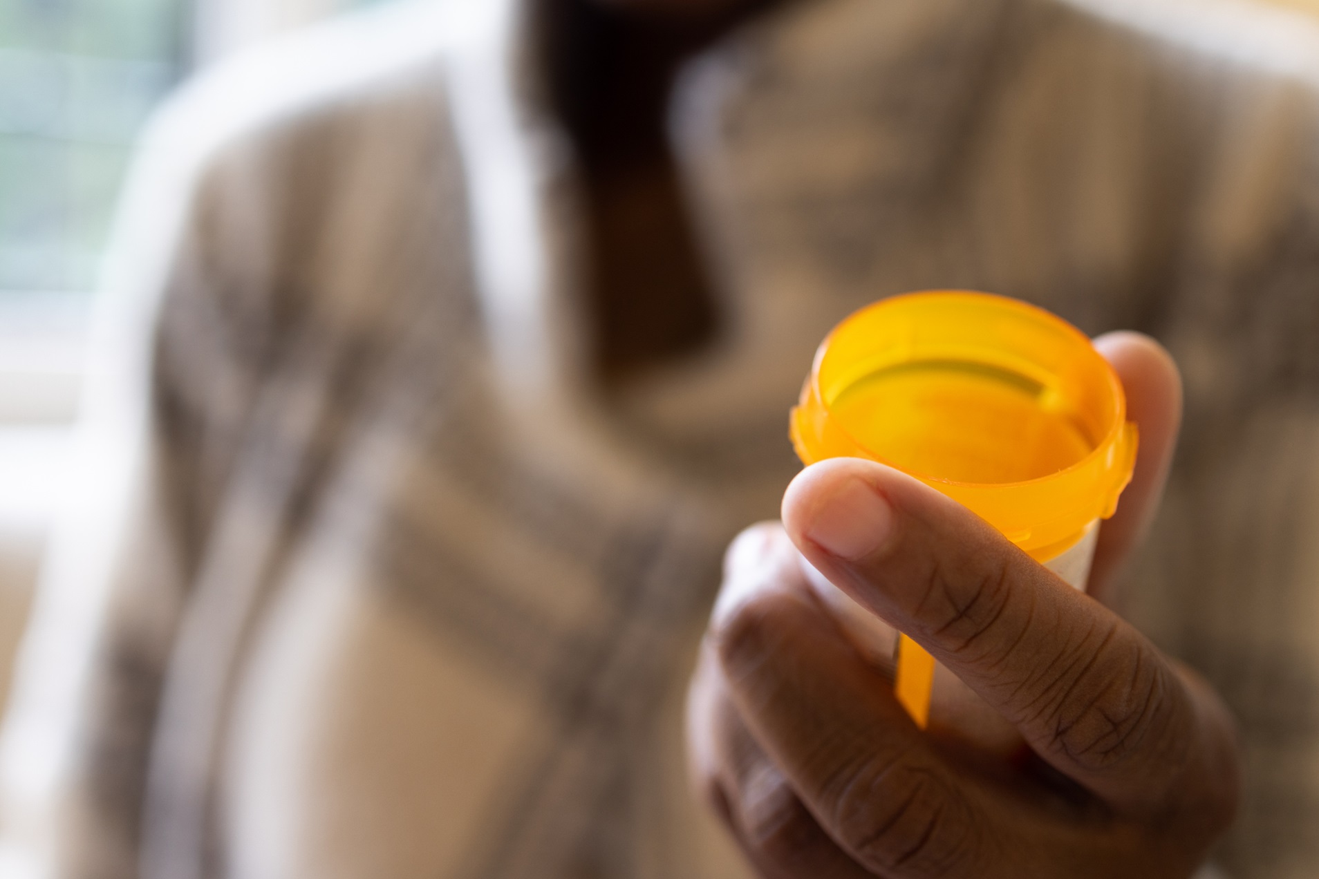 Man's hand in foreground holding empty prescription bottle