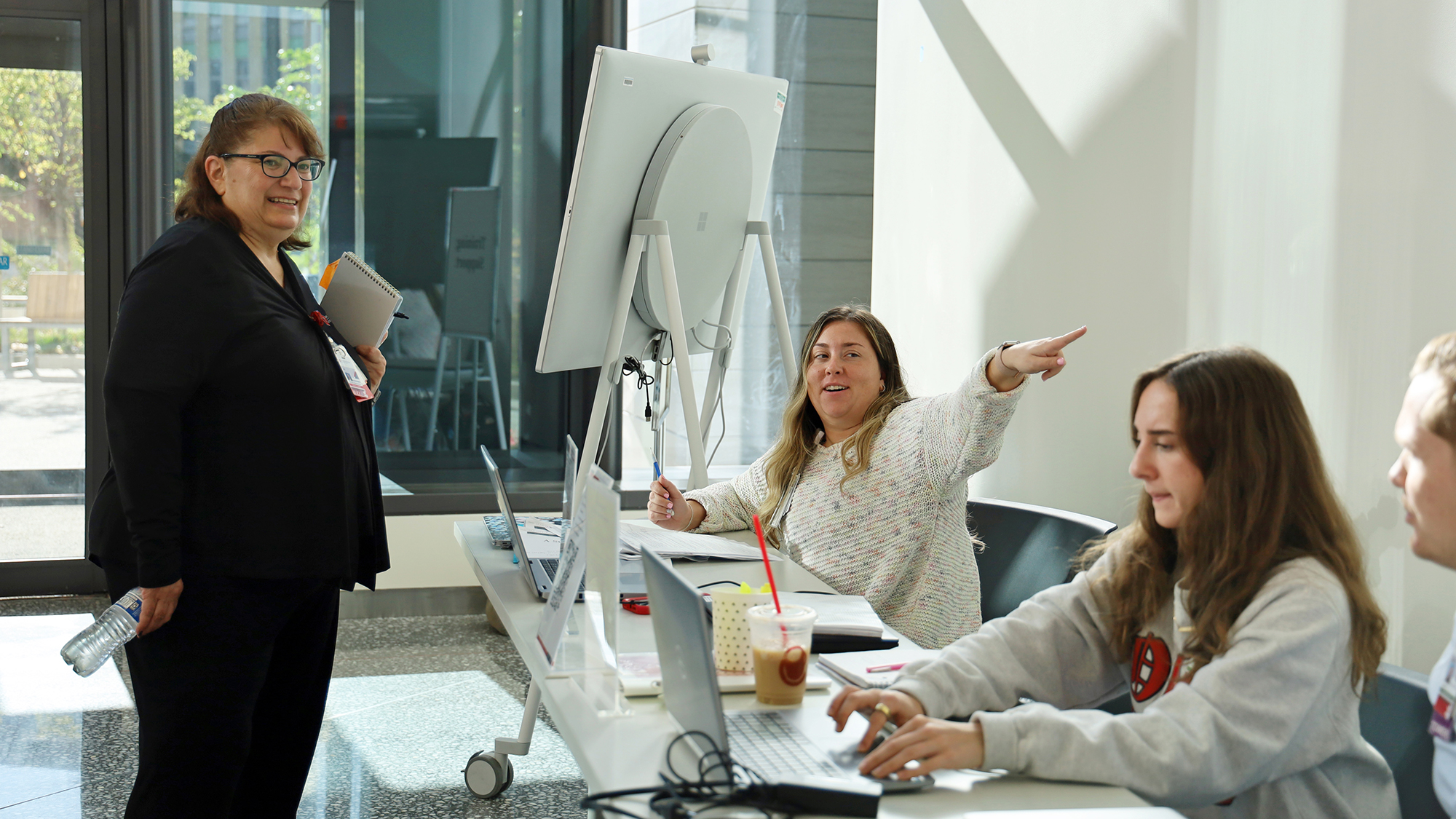 A student provides directions to a hospital employee while another student types on a laptop