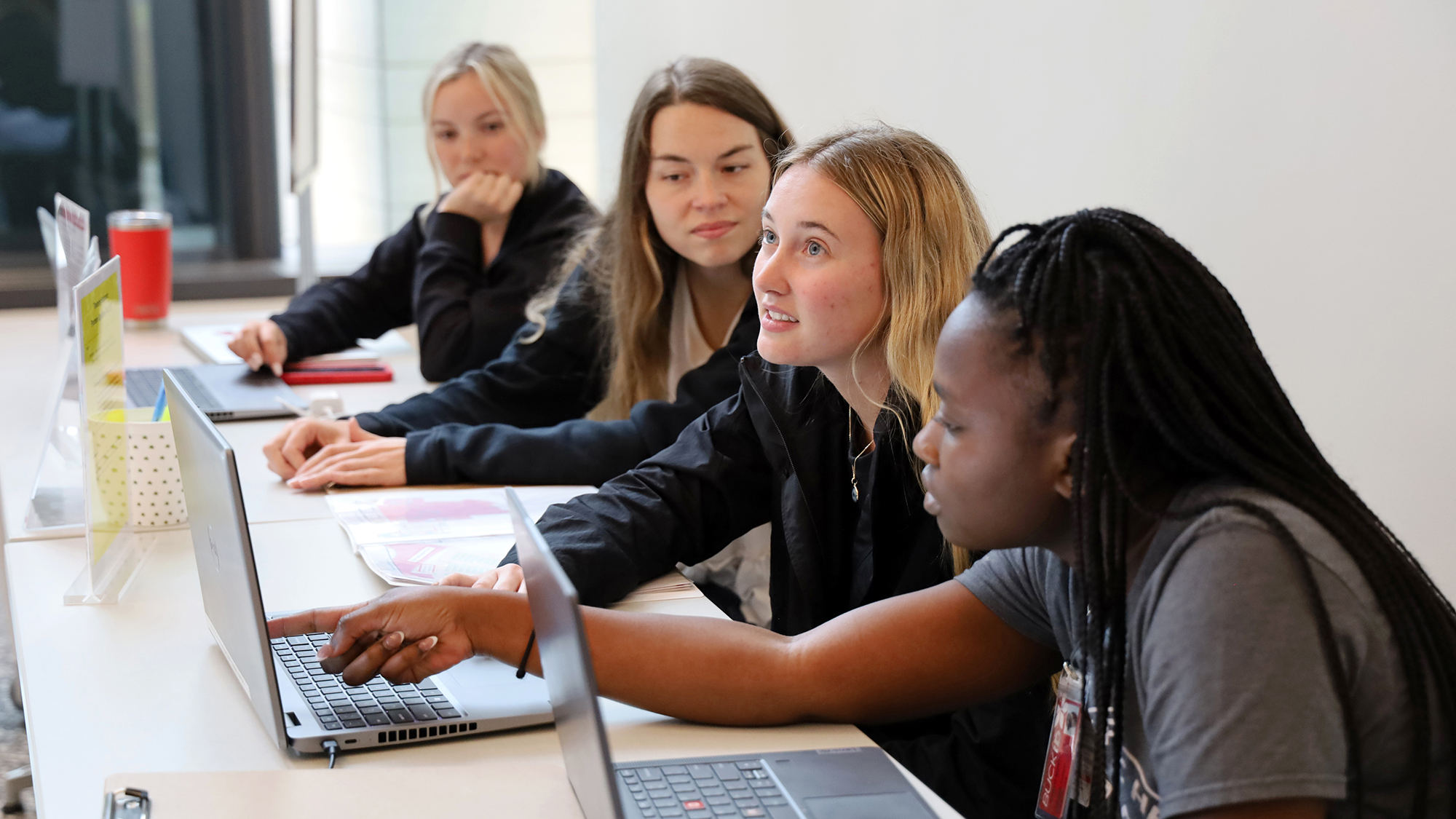 four students sit at a table behind laptops