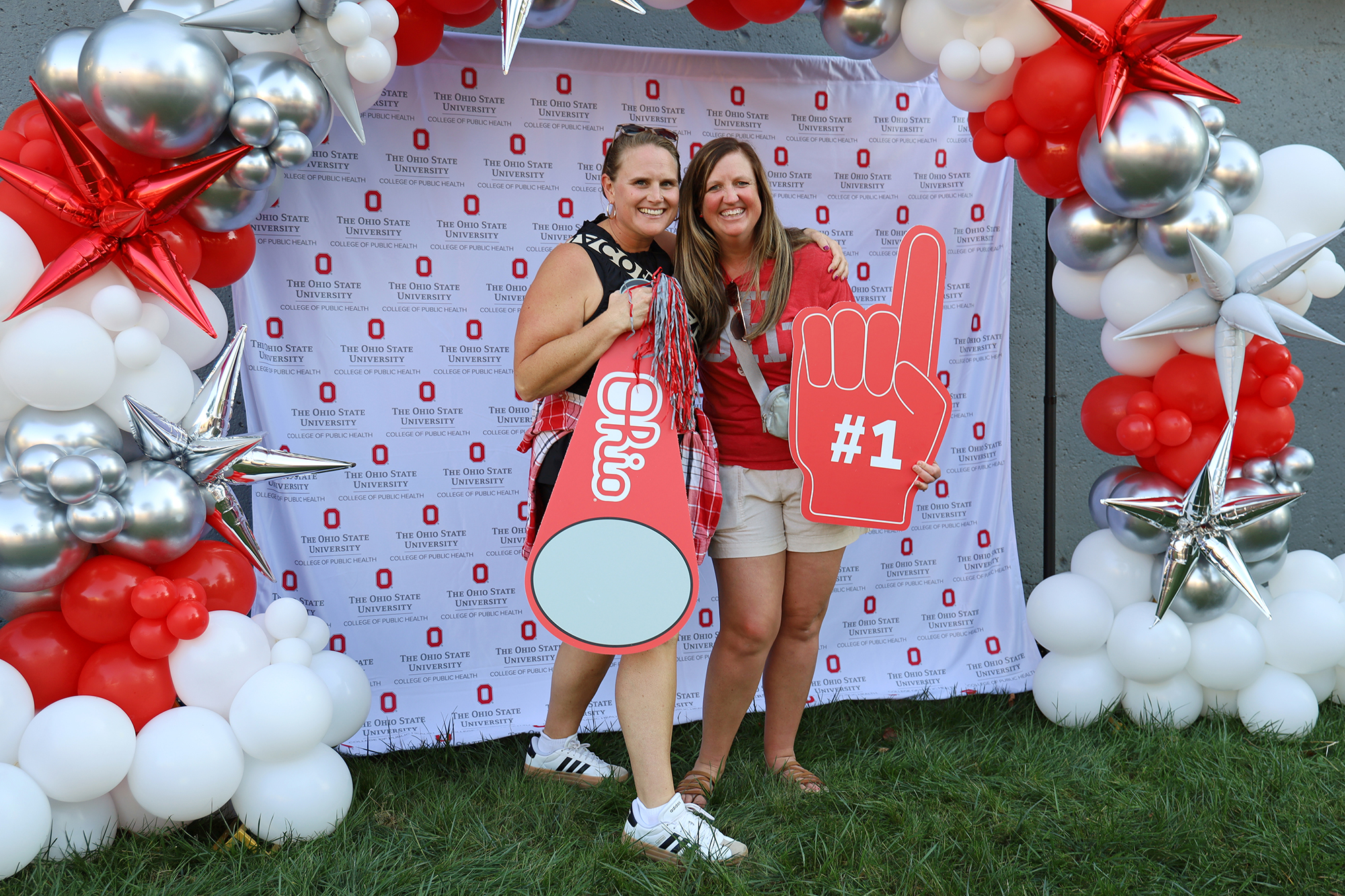 two people pose in front of a College of Public Health balloon display