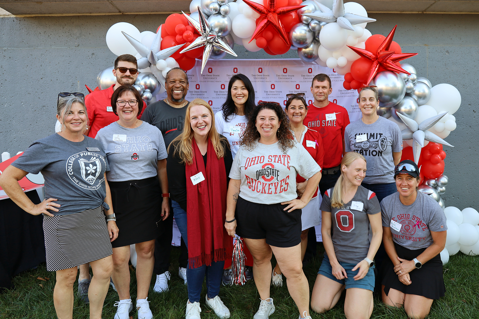 a group of people smile outside with balloons in the background. They are wearing Buckeye attire.