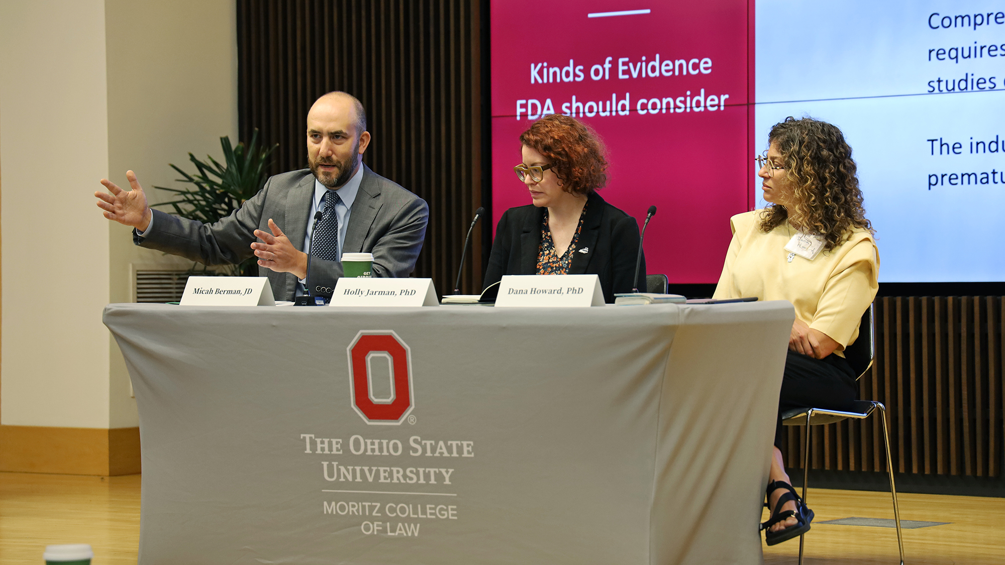 Three people sit at a table. One person is gesturing with his hands.