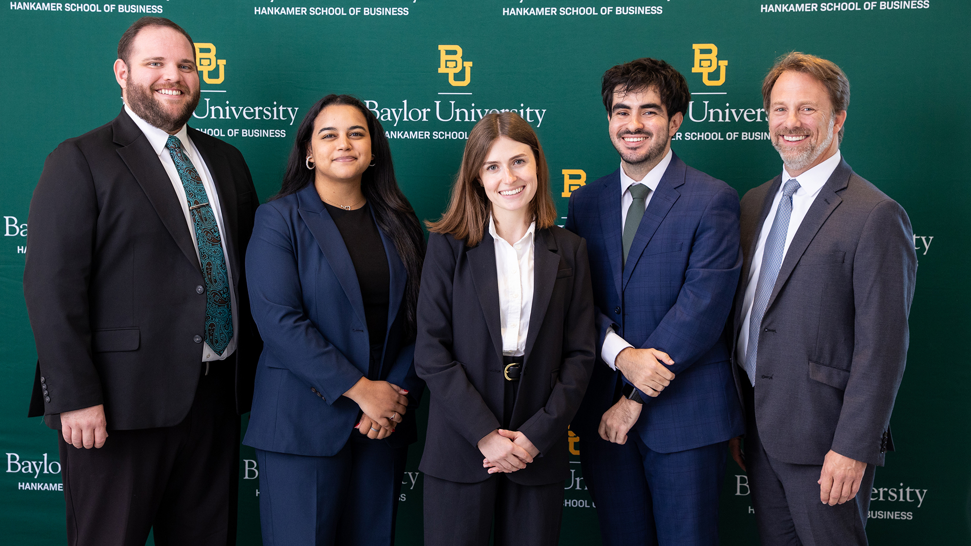 five people in business attire stand in front of a green background that says "Baylor University."