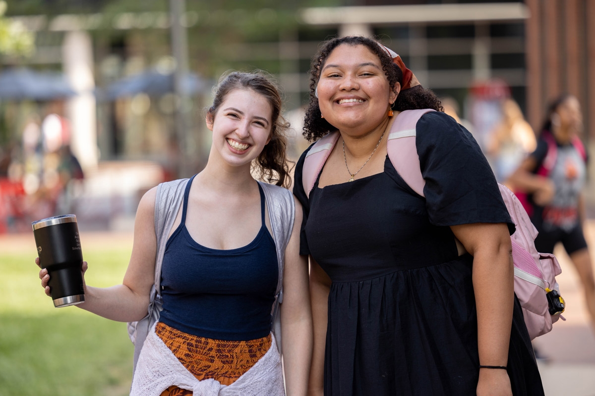 Two smiling young women wearing backpacks standing near each other