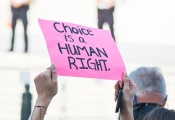 a person raising their arms with a pink sign that reads Choice is a human right.