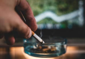 a person holds a cigarette over an ash tray.