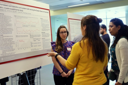 A student discussing their research poster to a group