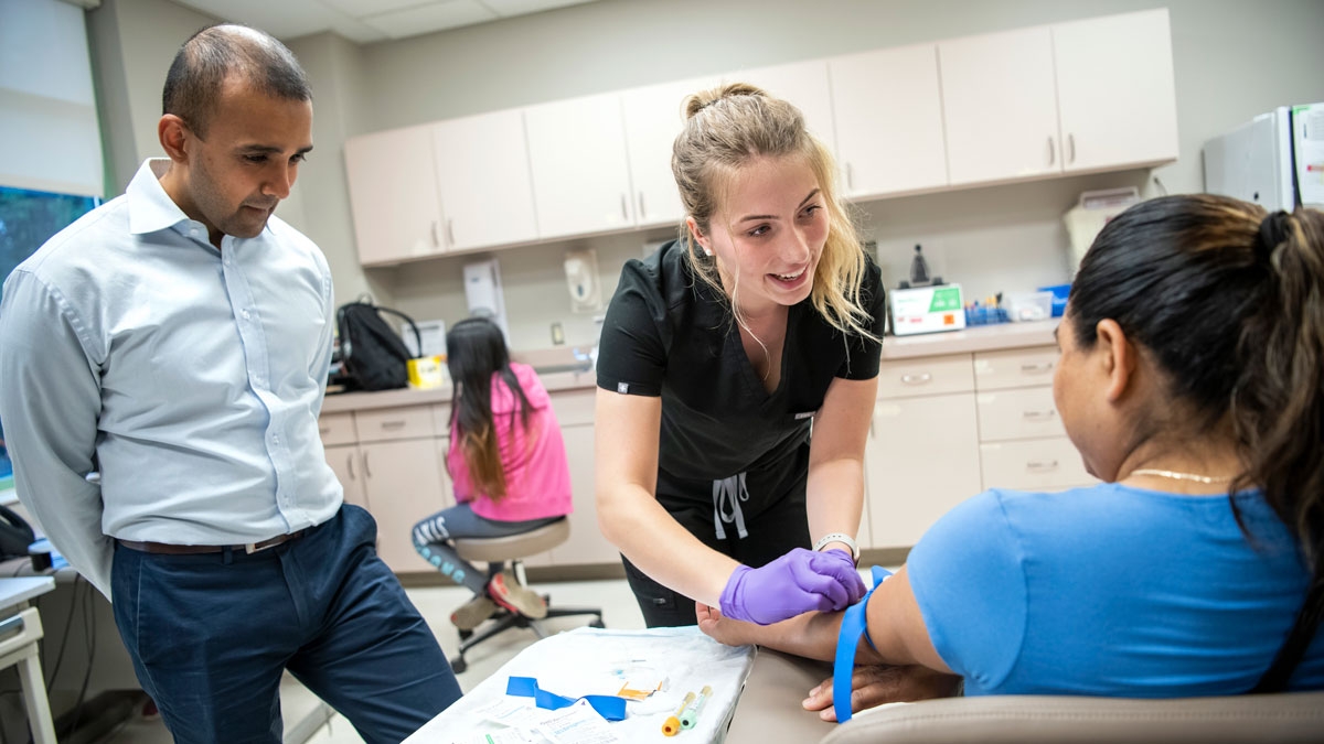 A public health nurse performs a test on a patient while a health care leader looks on