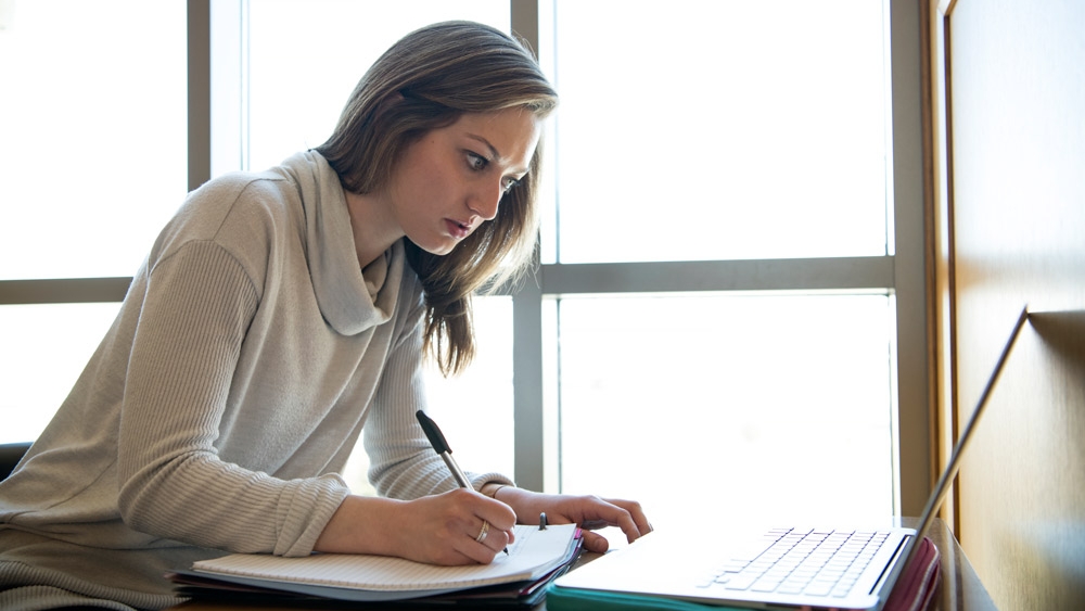 Student writing notes and looking at computer