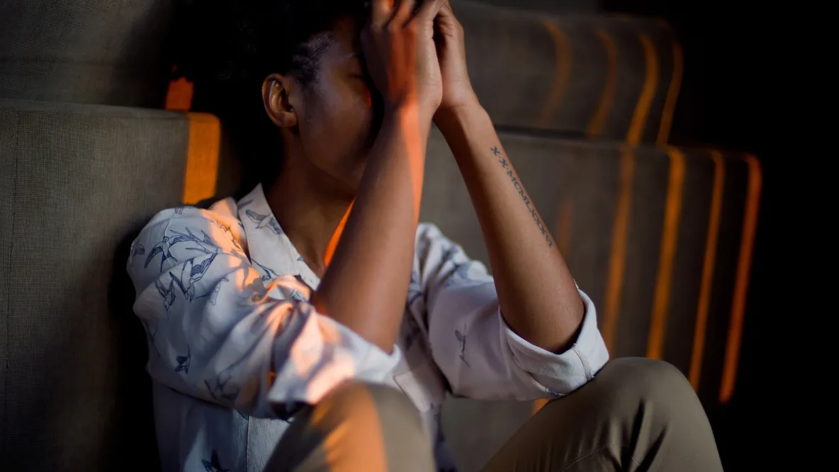A young person sitting down with their hands in front of their face, appearing distraught.