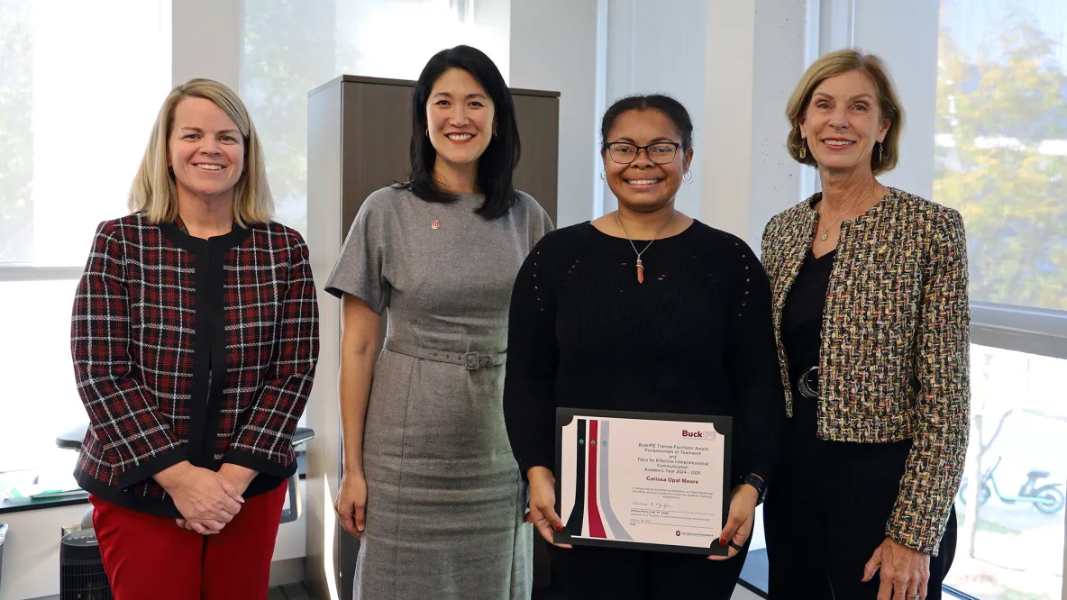 Four people smile. One person holds a certificate.