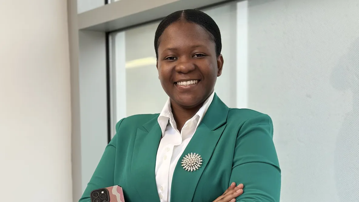 A student wearing a green blazer with a brooch and a white shirt smiles