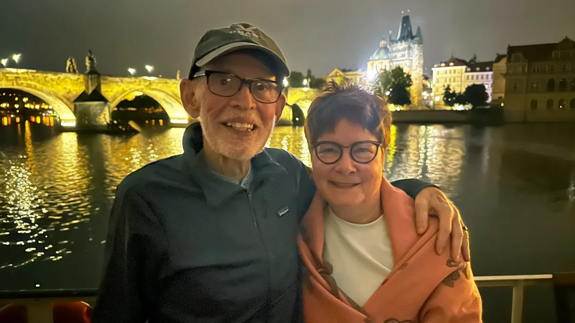 Larry and Barbara Margolis smile with a river and a brightly-lit bridge in the background.