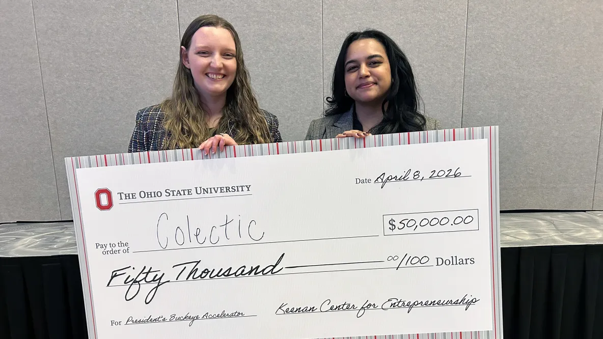 two students stand holding an oversized cheque.