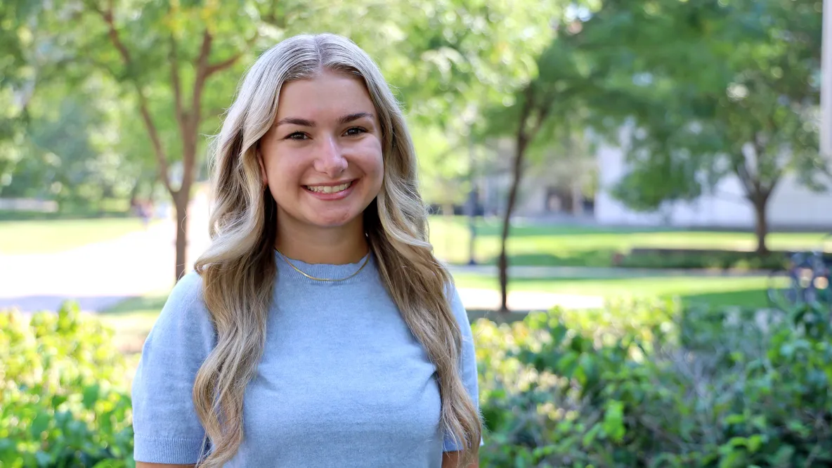 A student with long hair smiles outside.