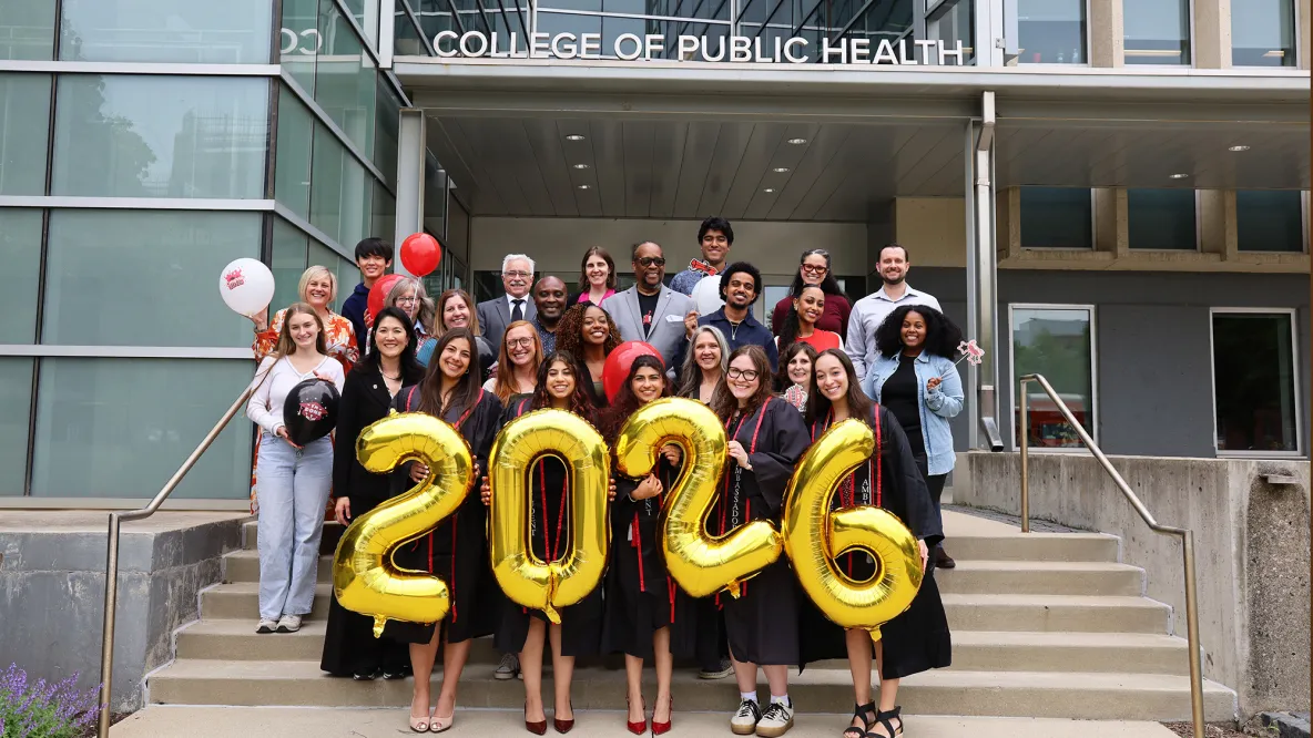 Students in graduation robes pose with balloons that spell "2-0-2-6" on the steps of Cunz Hall. They are joined by college faculty and staff.