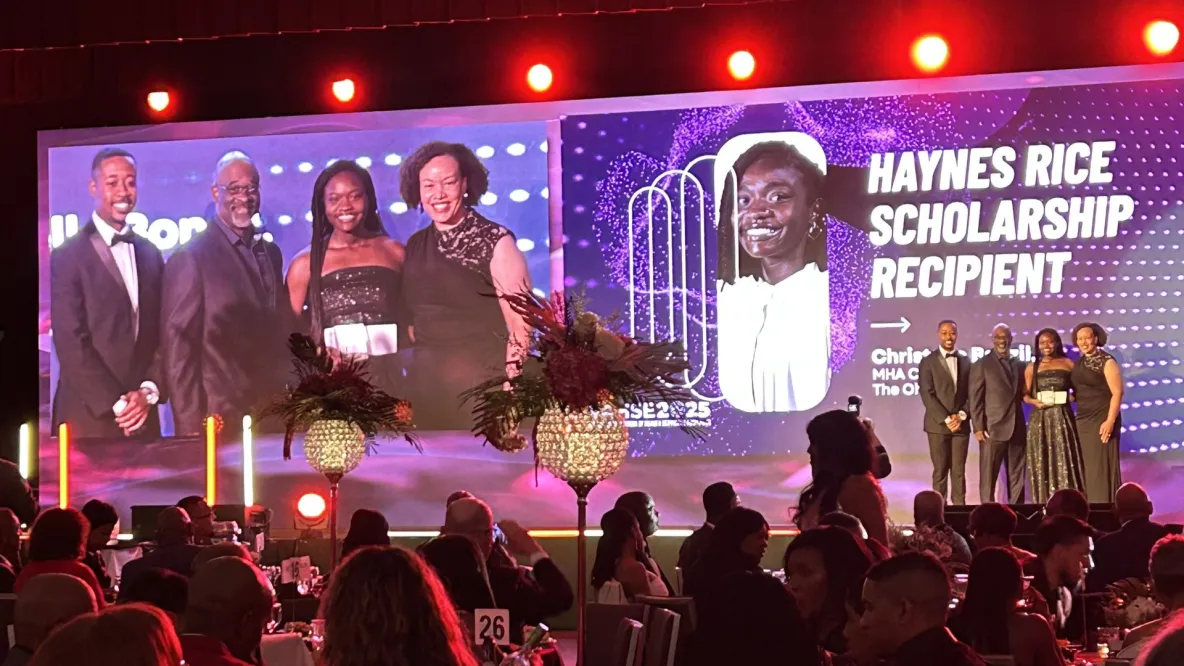 Four people stand on a stage in formal attire.